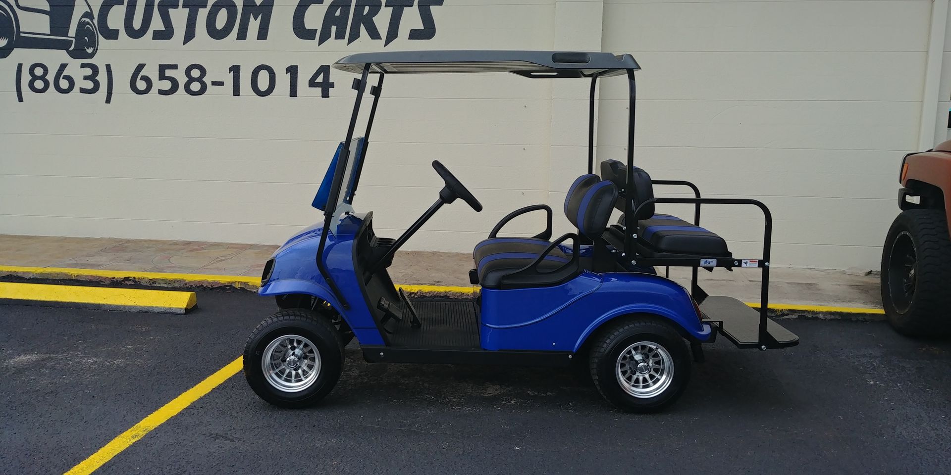 Blue golf cart parked outside, with a black roof and wheels, in front of a building with text that reads 