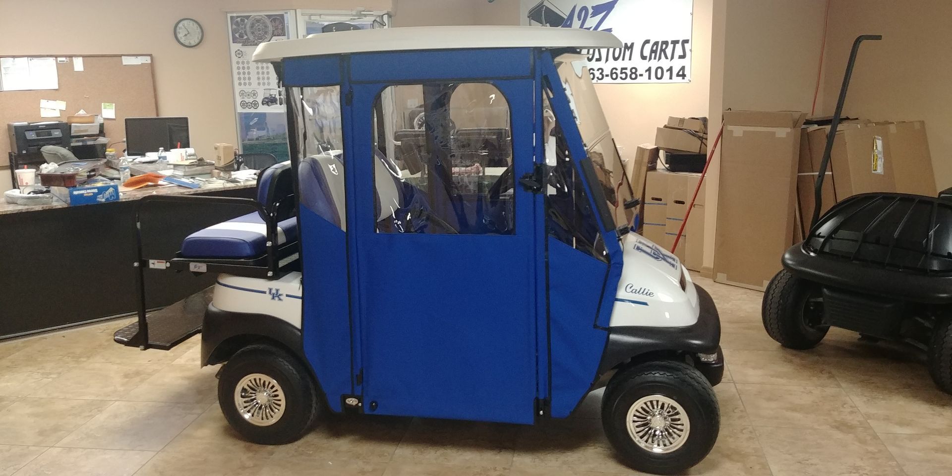 A blue and white golf cart with a roof, sitting inside a room.