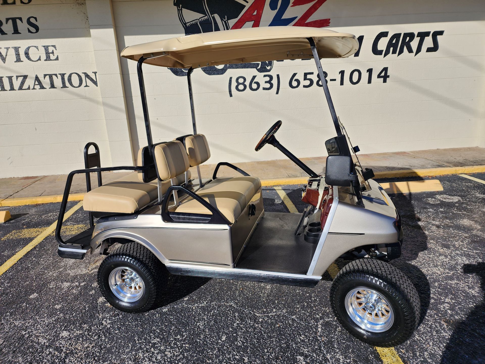 Tan and silver golf cart with a canopy parked outside a business.
