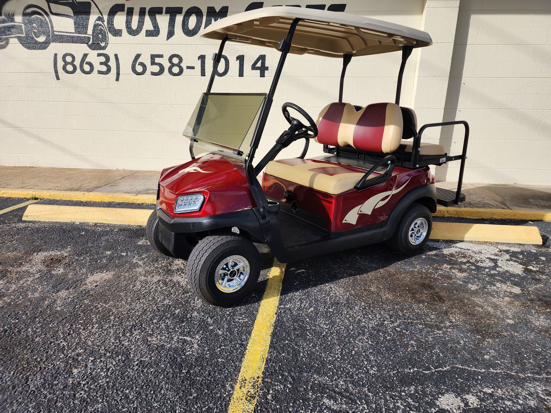 Red and tan golf cart parked outside a business with the phone number (863) 658-1014.
