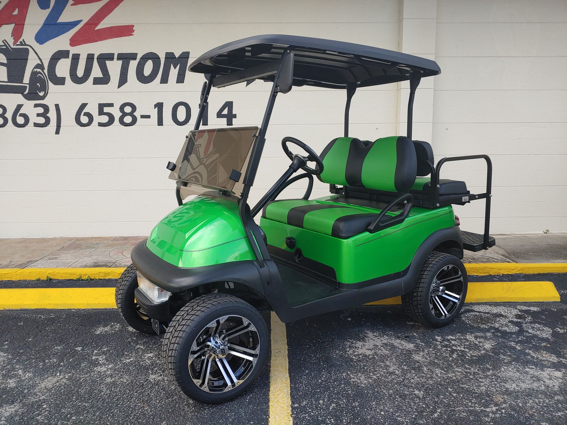 Green and black custom golf cart with black wheels, parked in front of a store.