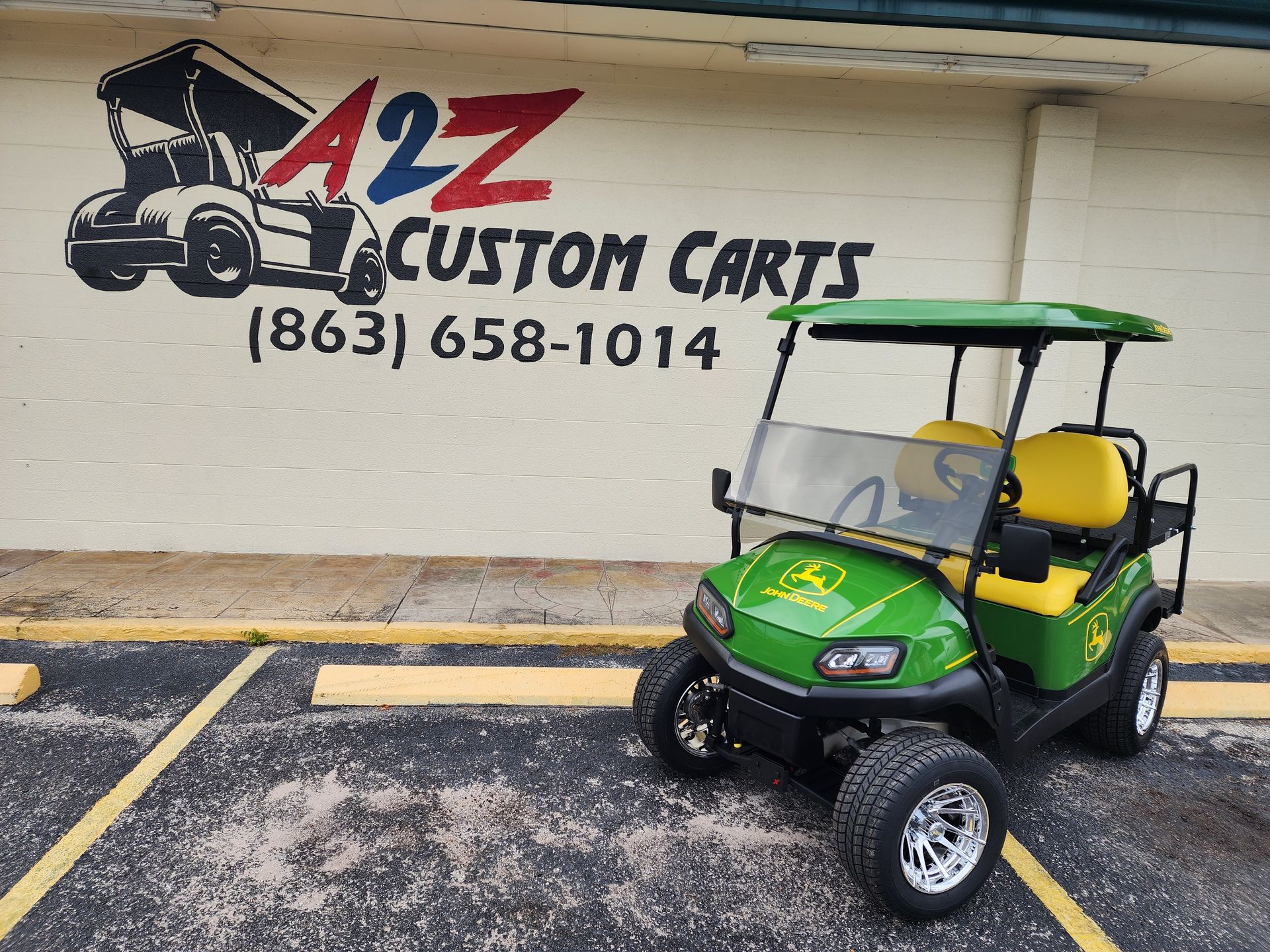 Green and yellow John Deere golf cart parked in front of A2Z Custom Carts sign.