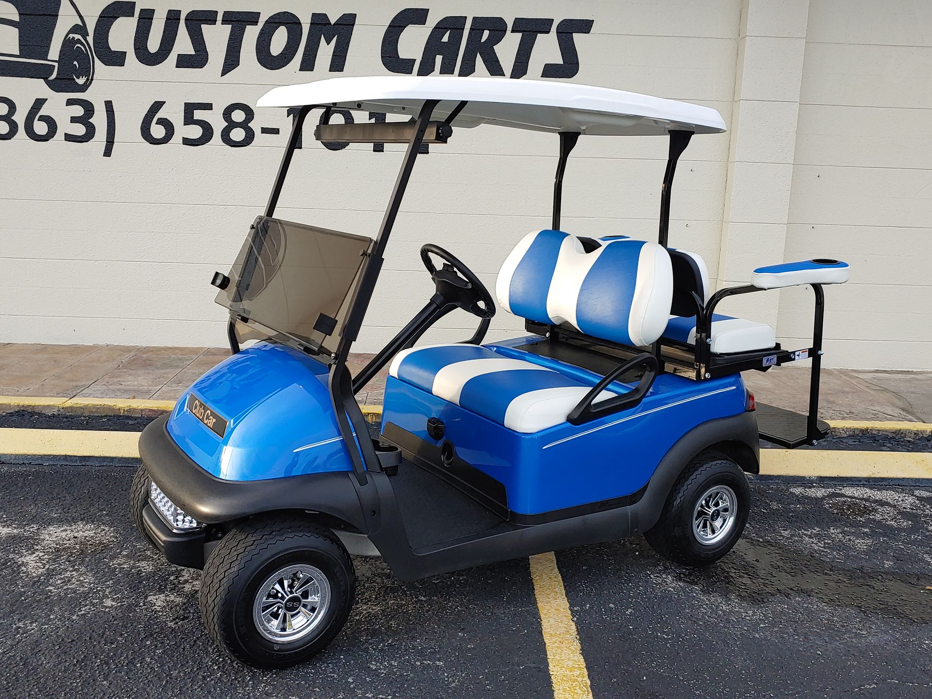 Blue and white golf cart with a white roof in front of a building.