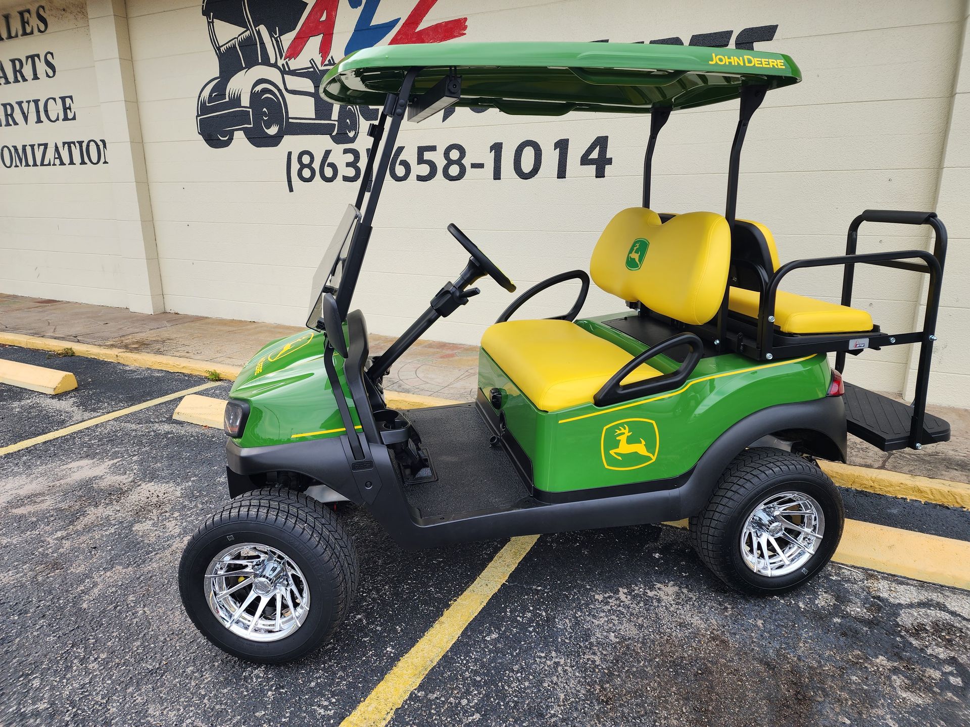 Green and yellow John Deere golf cart with chrome wheels parked outdoors.