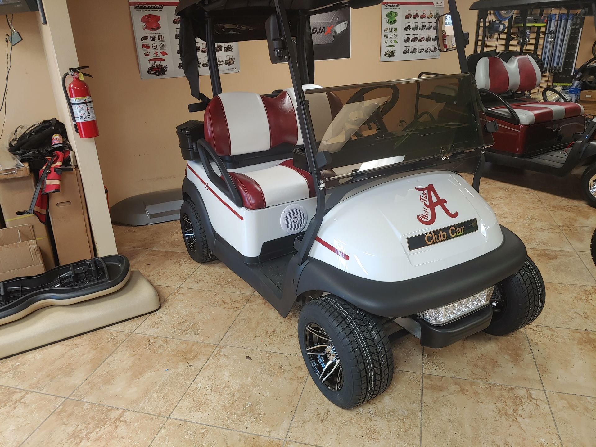 White golf cart with Alabama Crimson Tide logo, maroon and white seats, black wheels, and a fire extinguisher.