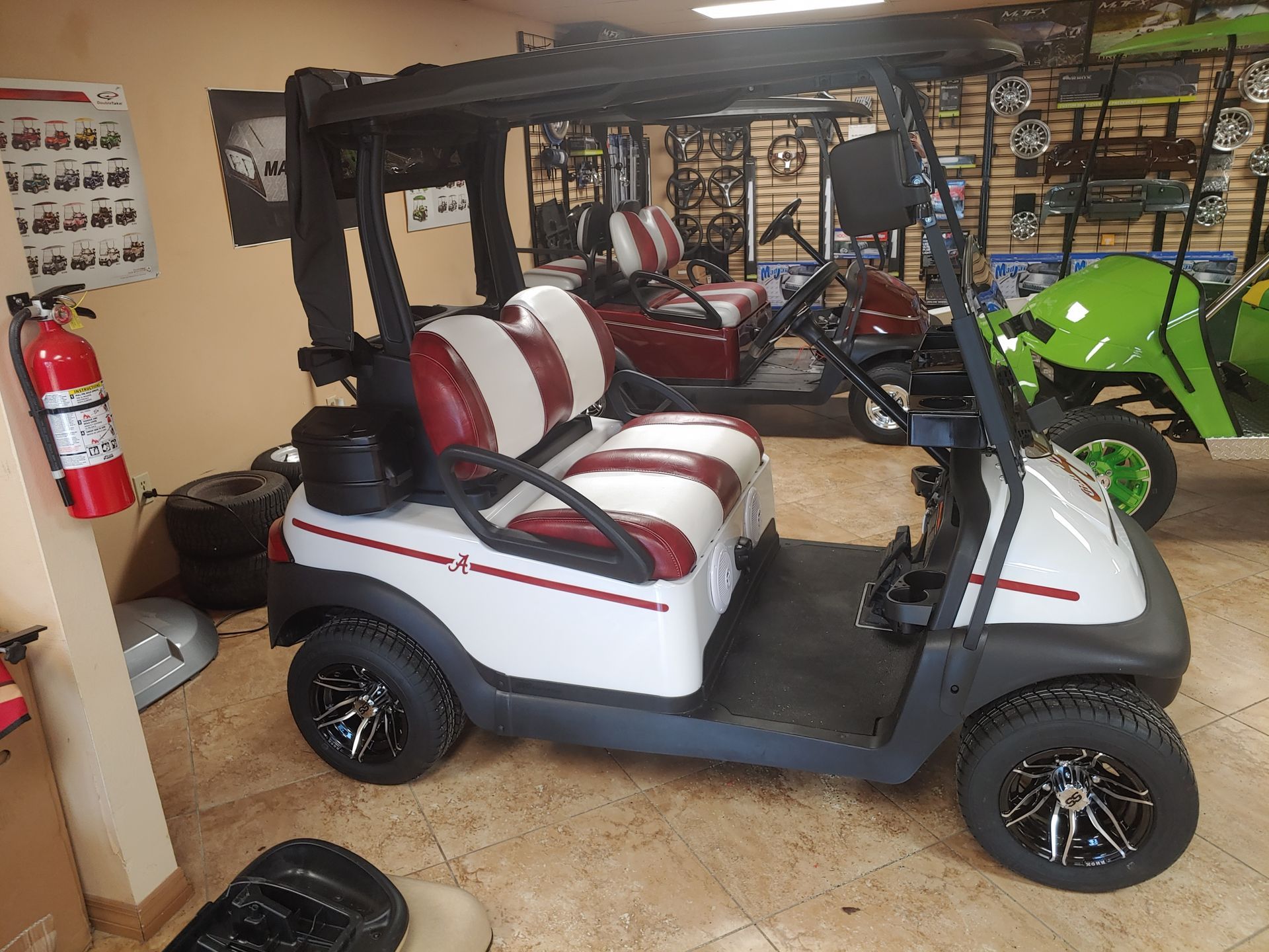 White golf cart with red and white seats, parked indoors. Other golf carts are in the background.
