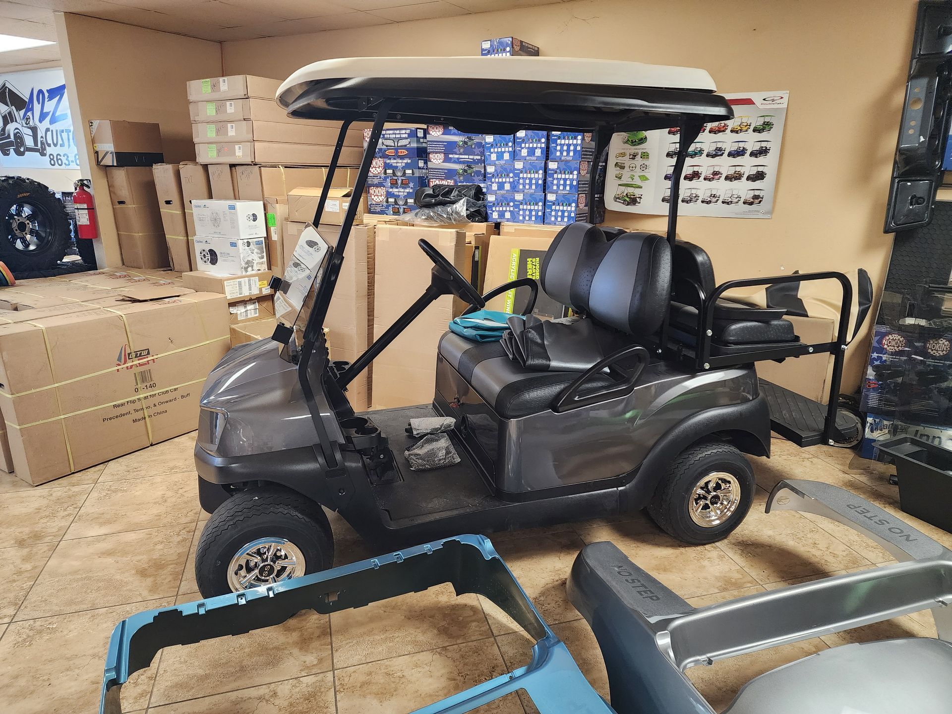 Gray golf cart inside a room with boxes and parts.