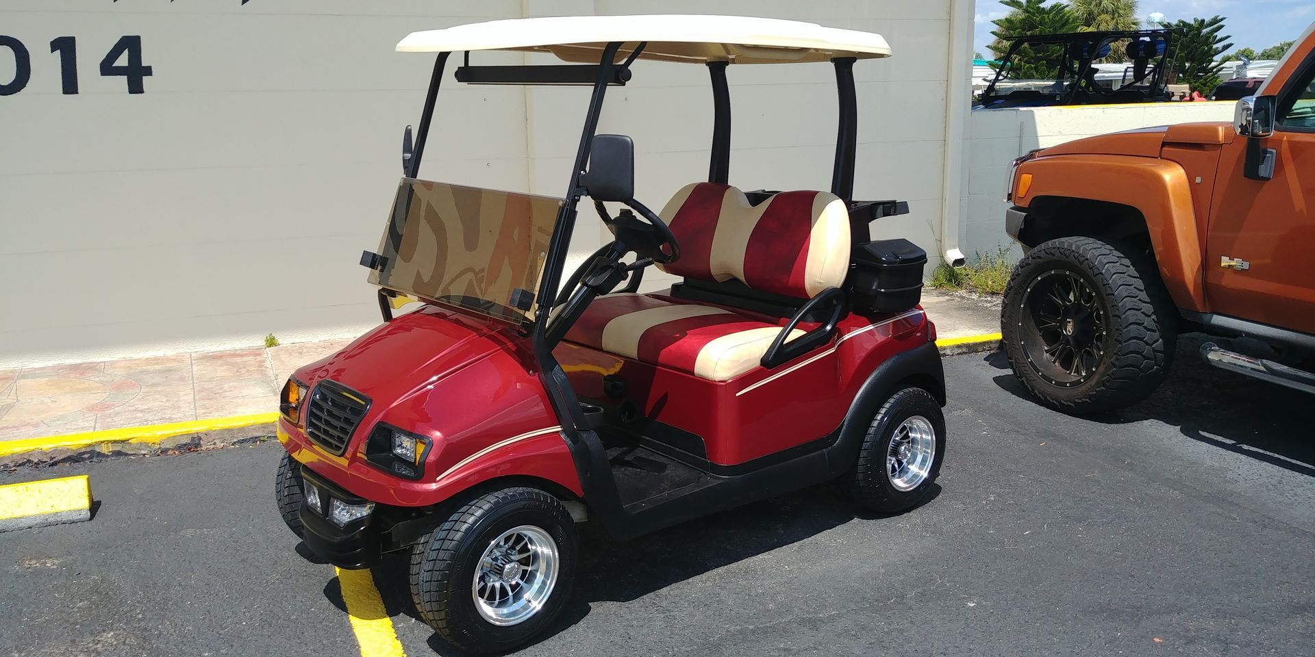 Red golf cart parked next to an orange SUV in a parking lot.