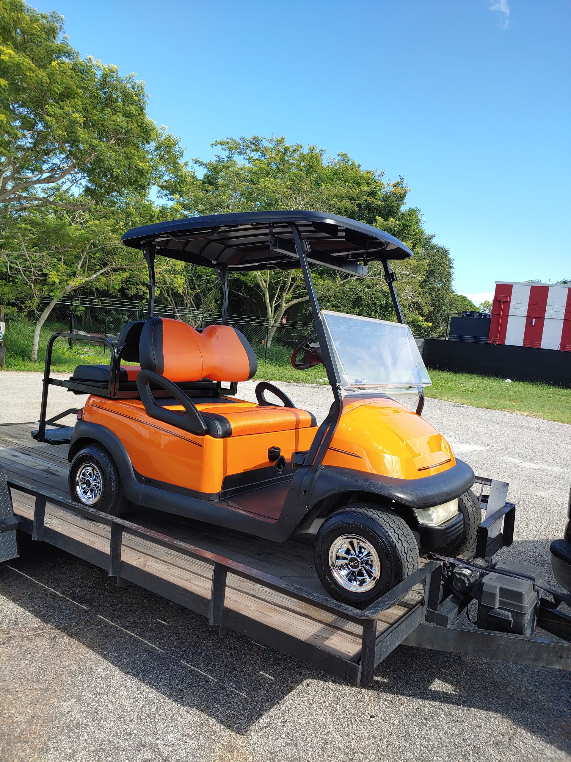 Orange golf cart on a trailer, black roof, brown seats, parked outdoors.