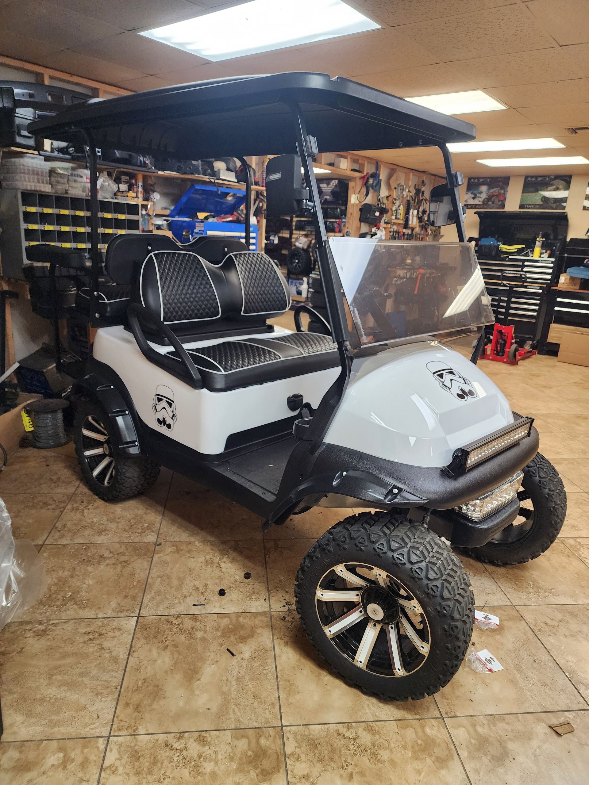 White and black golf cart with off-road tires in a garage.