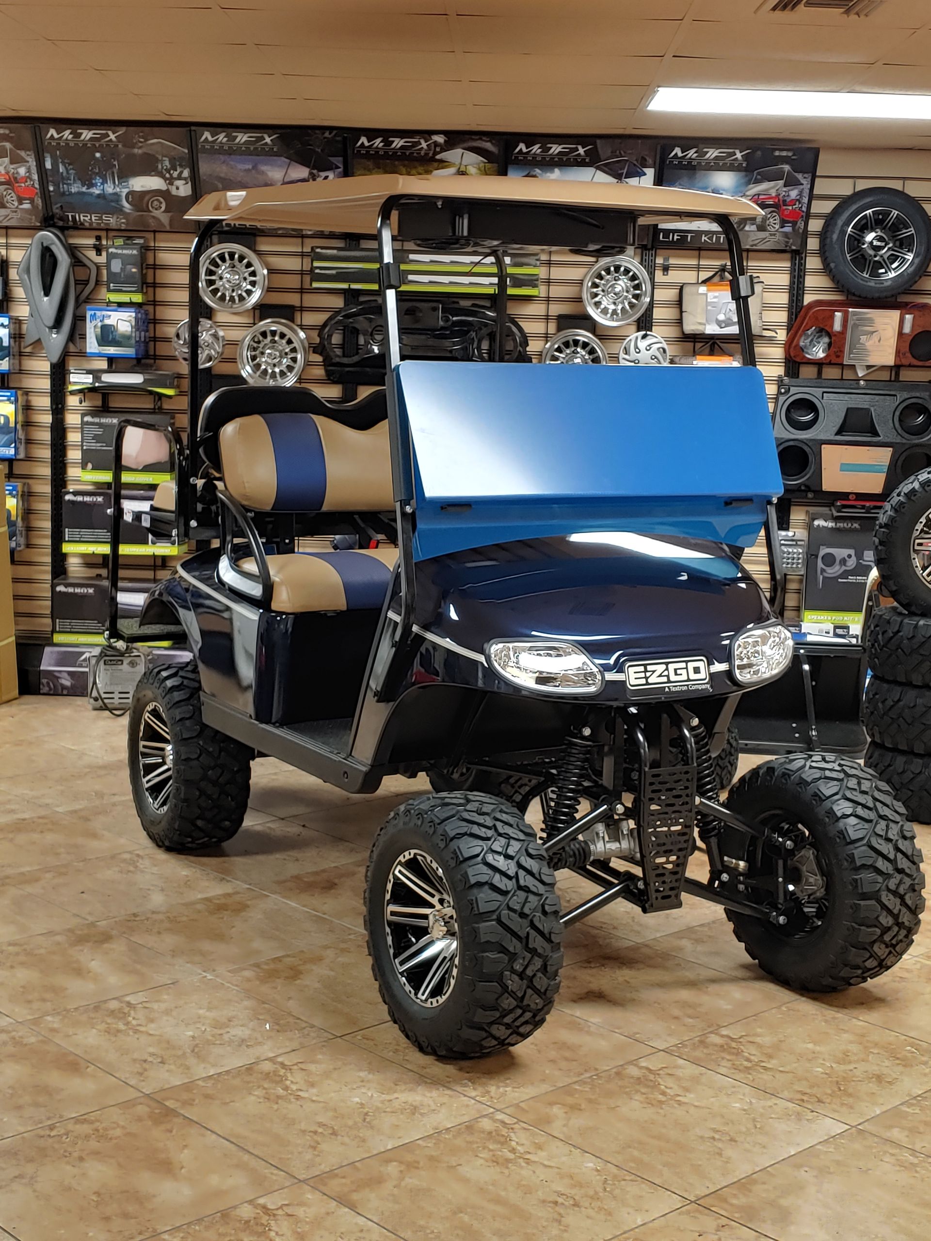 Black golf cart with blue windshield, brown top, and lifted tires in a shop.