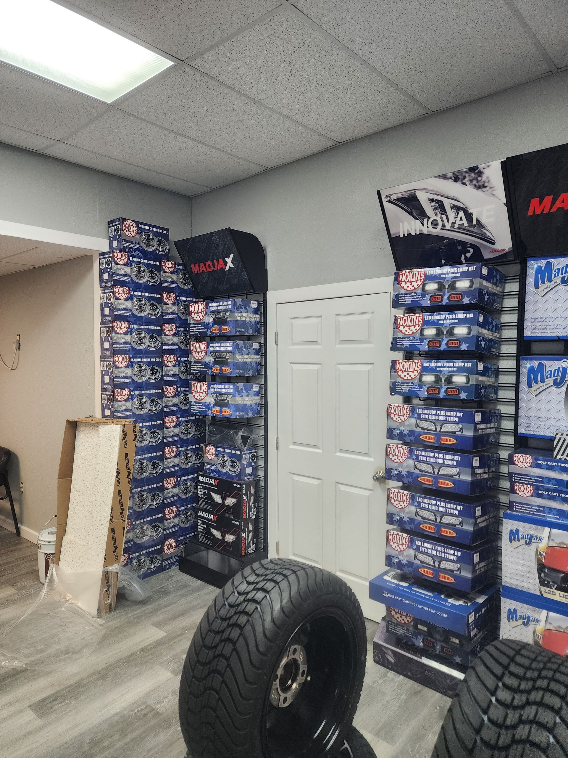 Inside a tire shop, stacks of blue and red boxes on shelves, tires in foreground.
