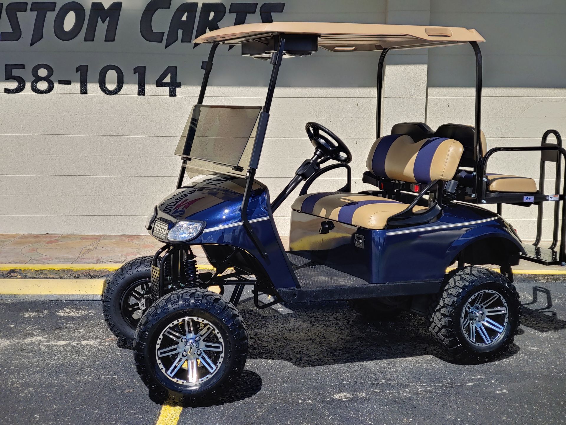 Blue and beige golf cart with off-road tires, parked in front of a building.