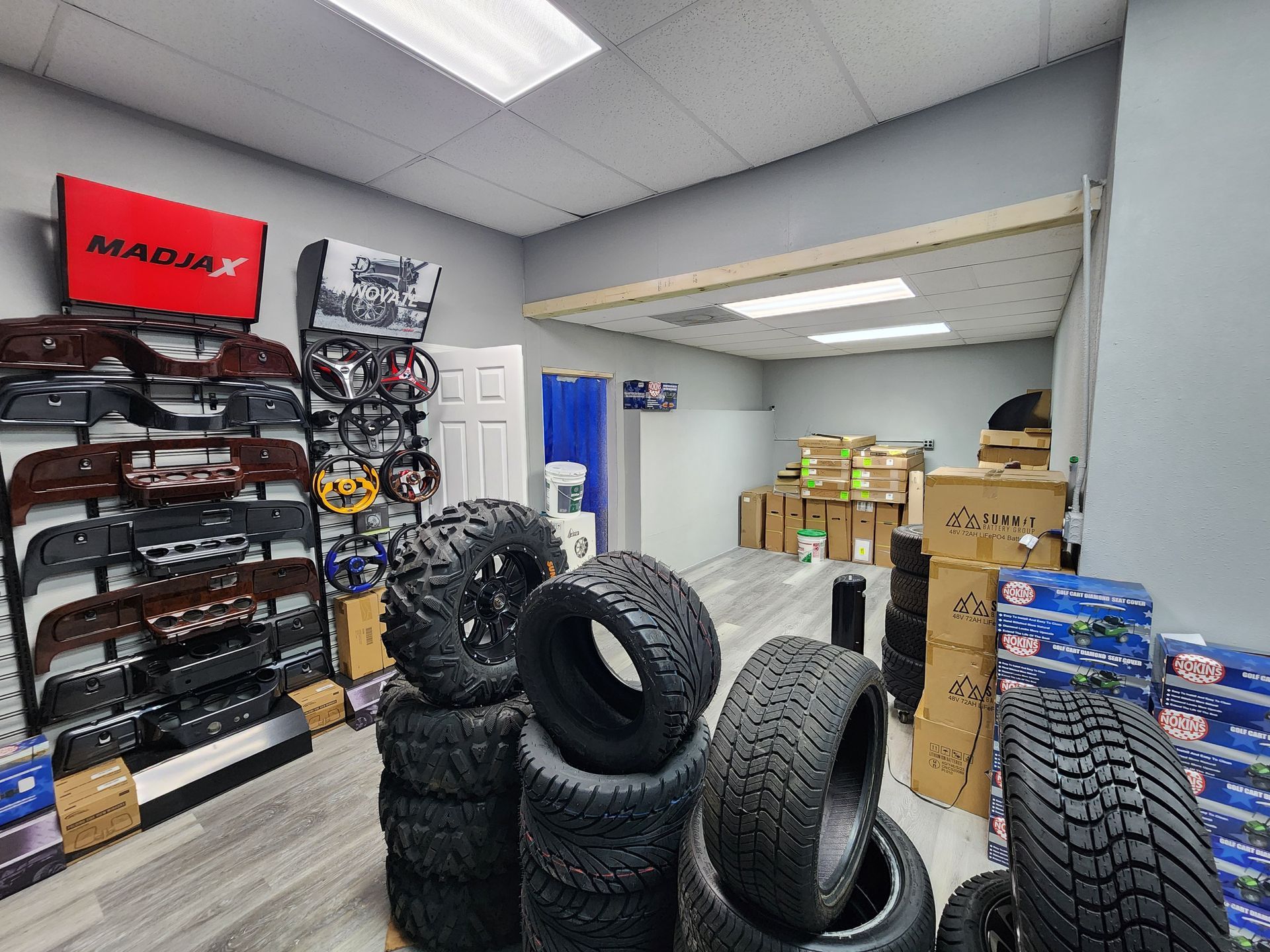 Tires stacked inside a shop with auto parts and boxes. A red sign is on the wall.