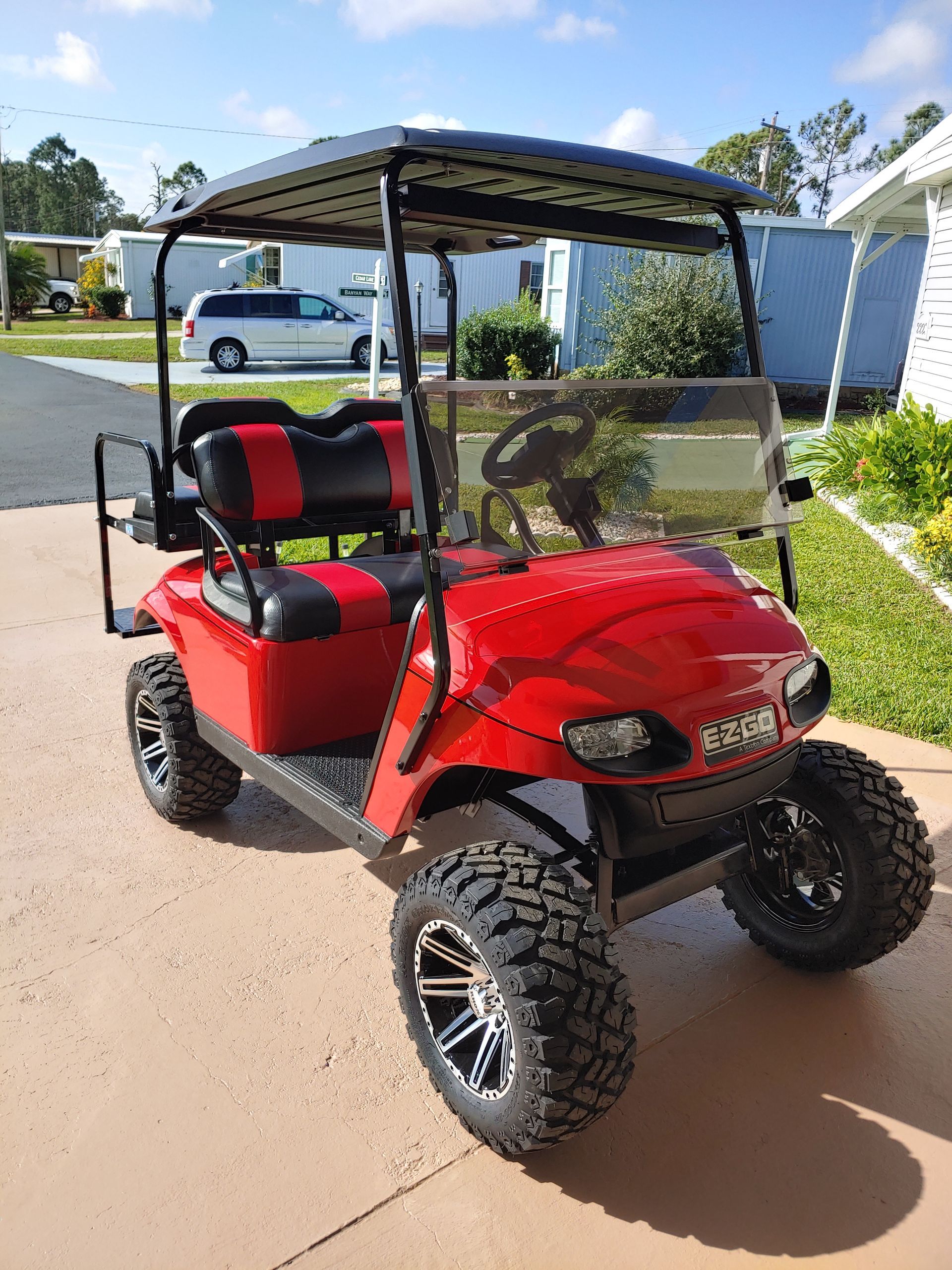 Red golf cart with black accents, large tires, and windshield parked outside on sunny day.