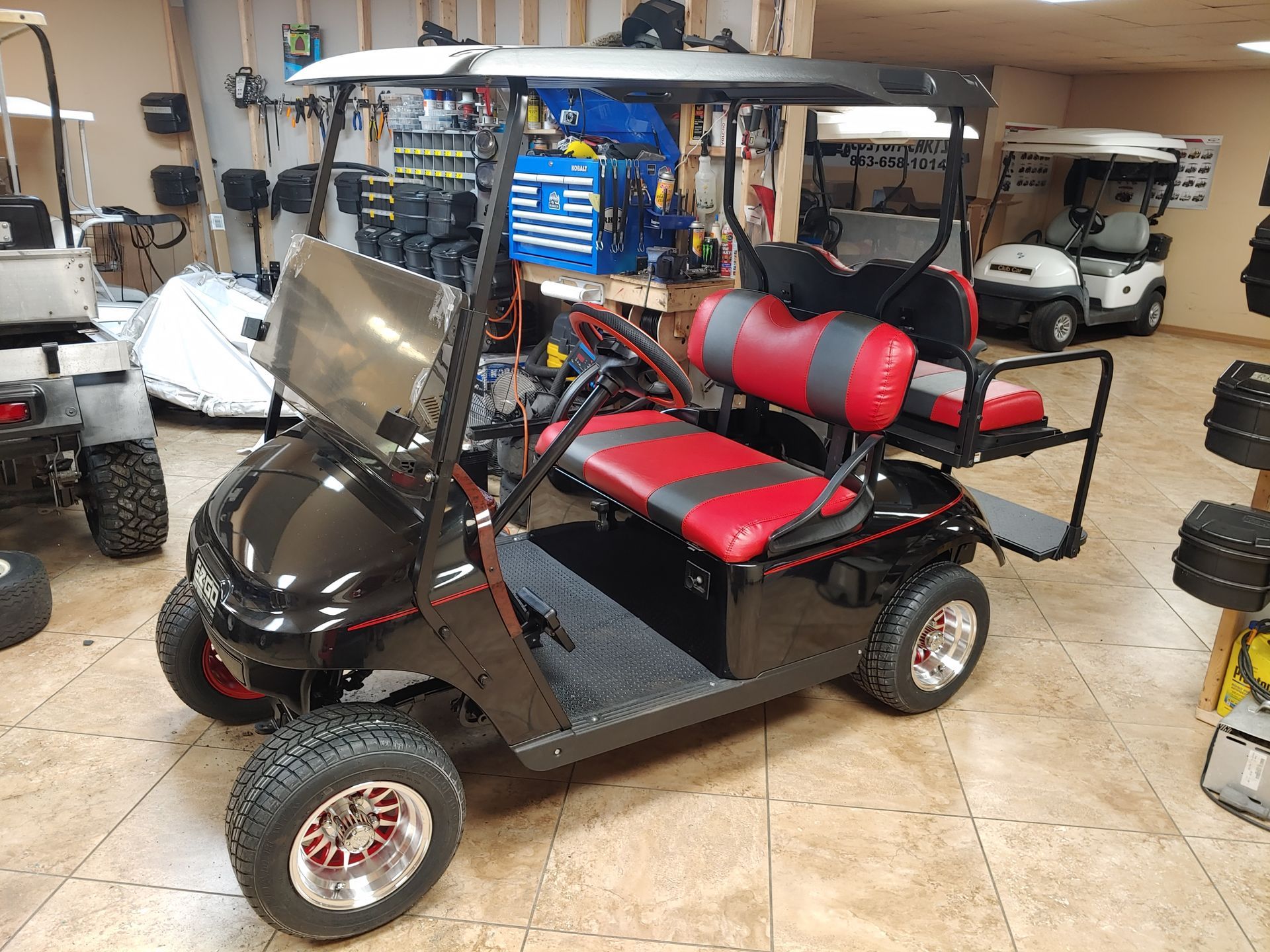 Black and red custom golf cart with off-road tires, parked in a showroom.