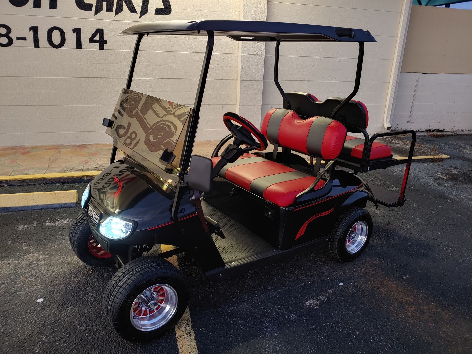 Black and red golf cart with a windshield, seats, and a canopy, parked outside.