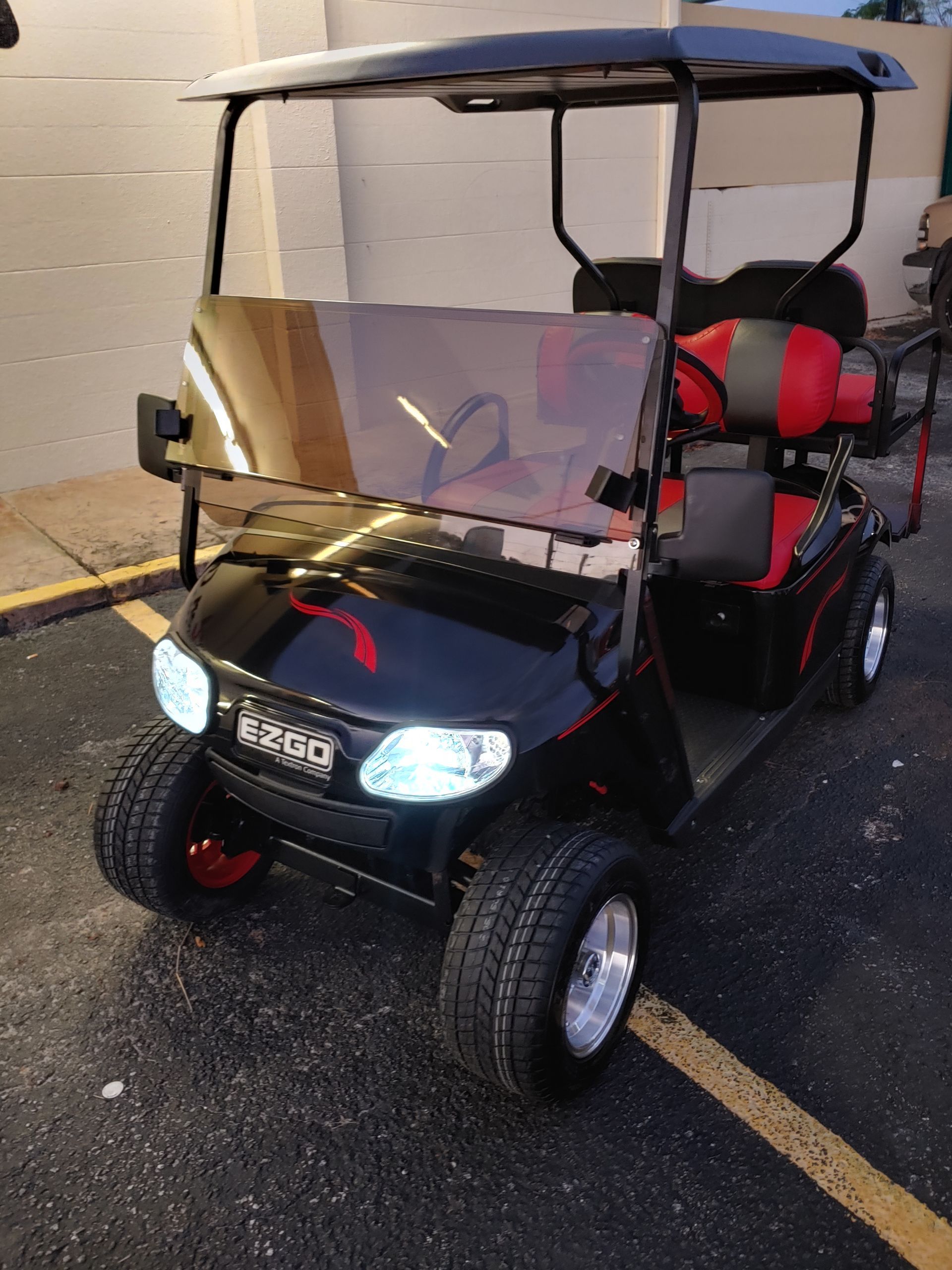 Black and red golf cart with a windshield, parked outdoors.