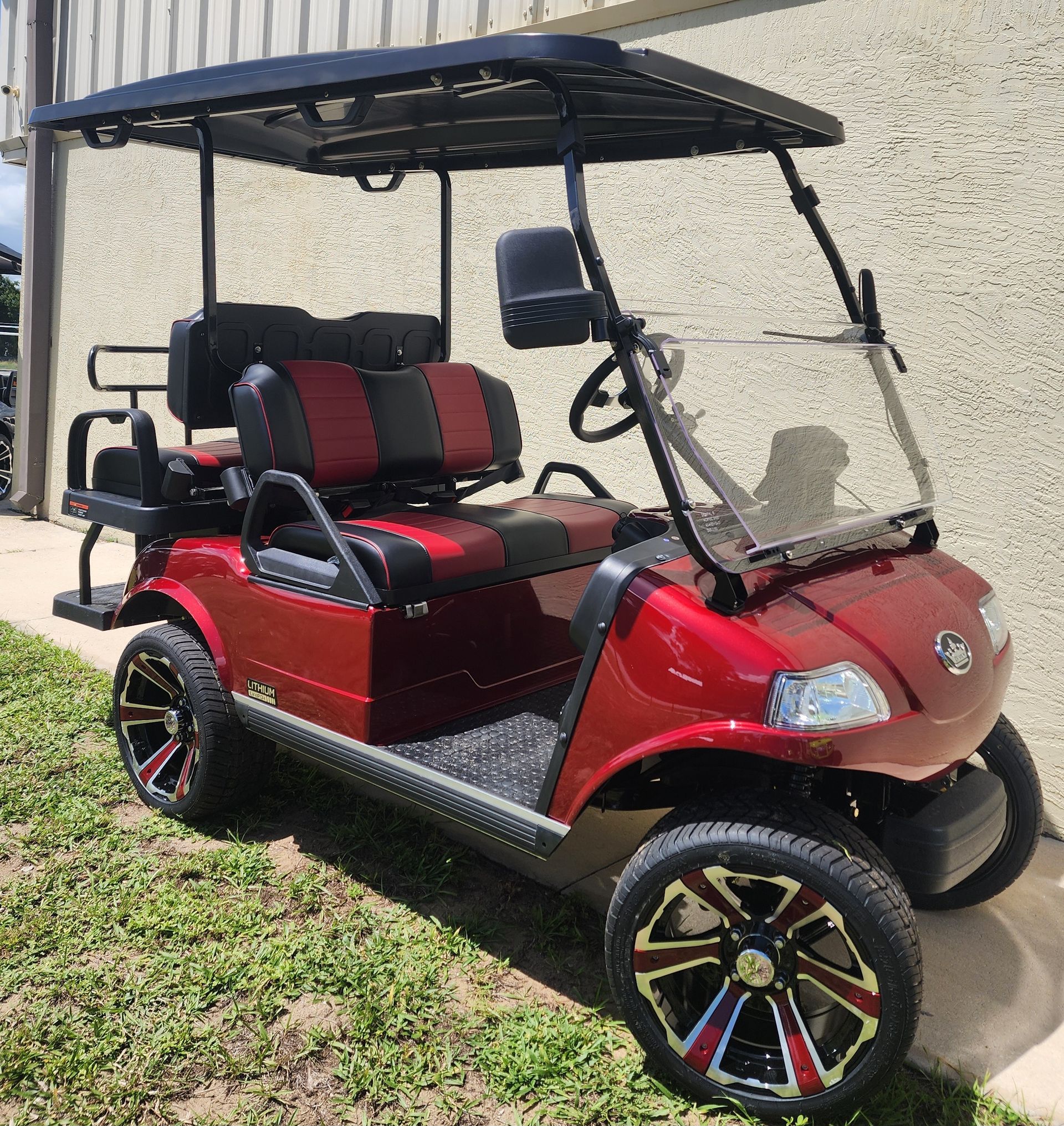 Red golf cart with black roof, seats, and custom wheels, parked on grass.