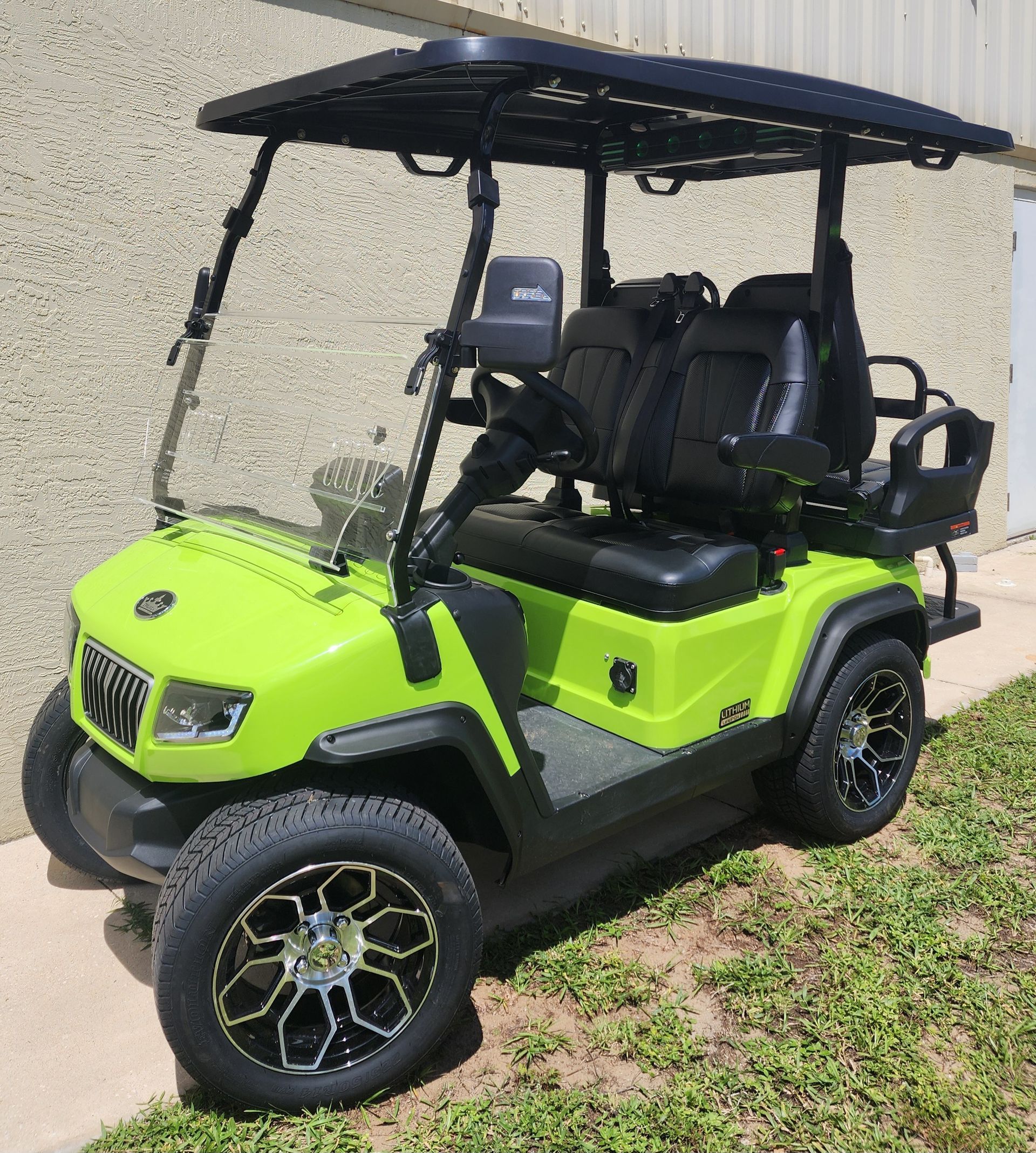 Bright green golf cart with black accents and black roof parked outdoors on grass.