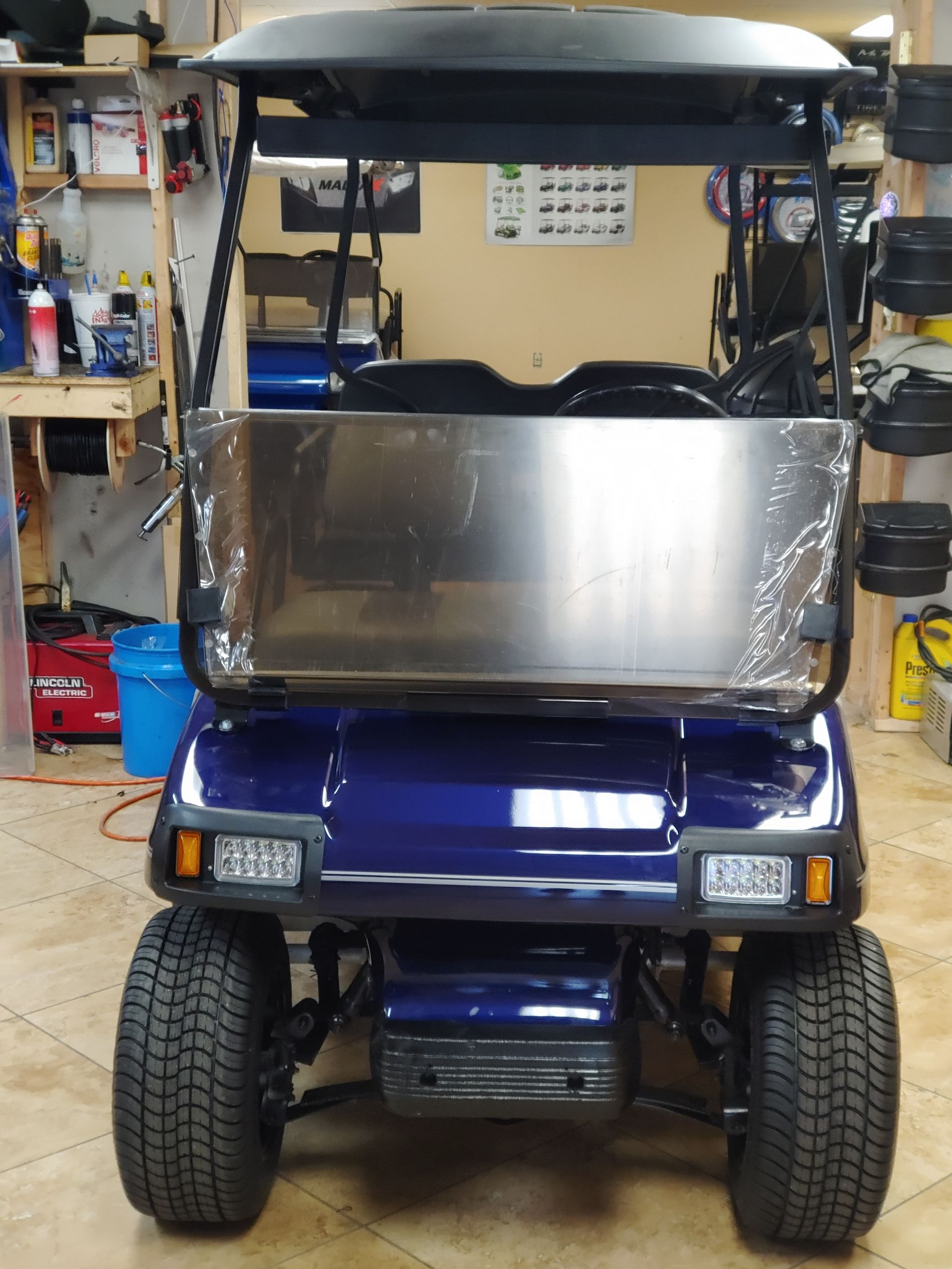 Blue golf cart with a windshield and black roof, parked in a garage.