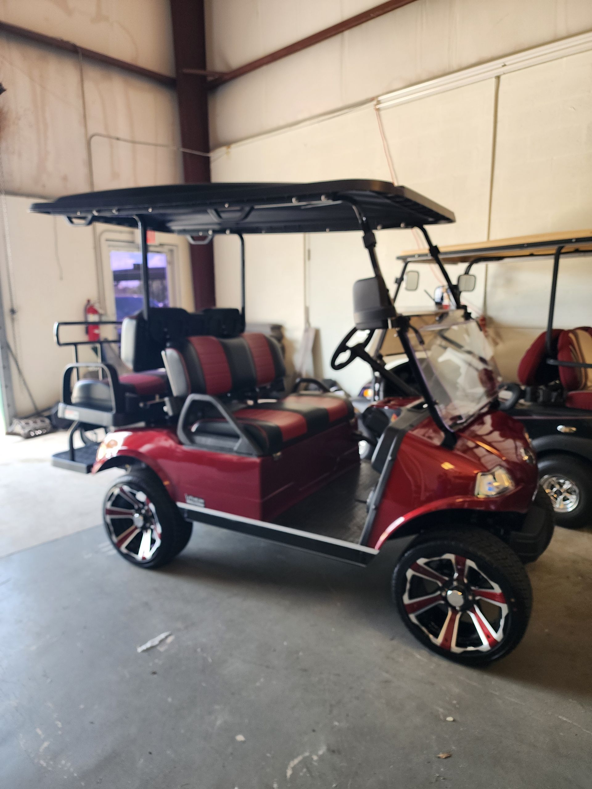 Red golf cart with black roof and seats, parked inside a garage.