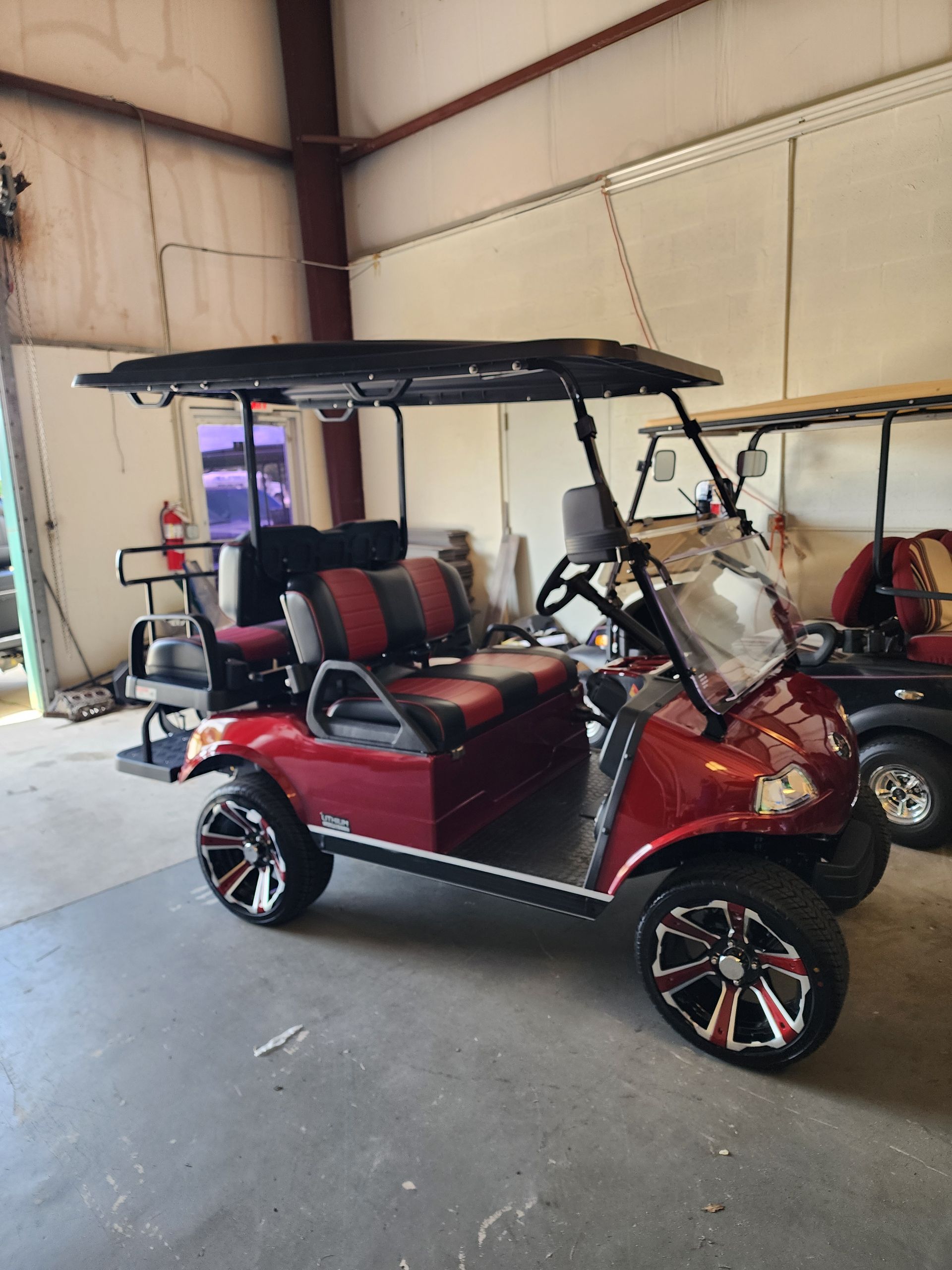 Red golf cart with black roof and custom wheels parked inside a building.