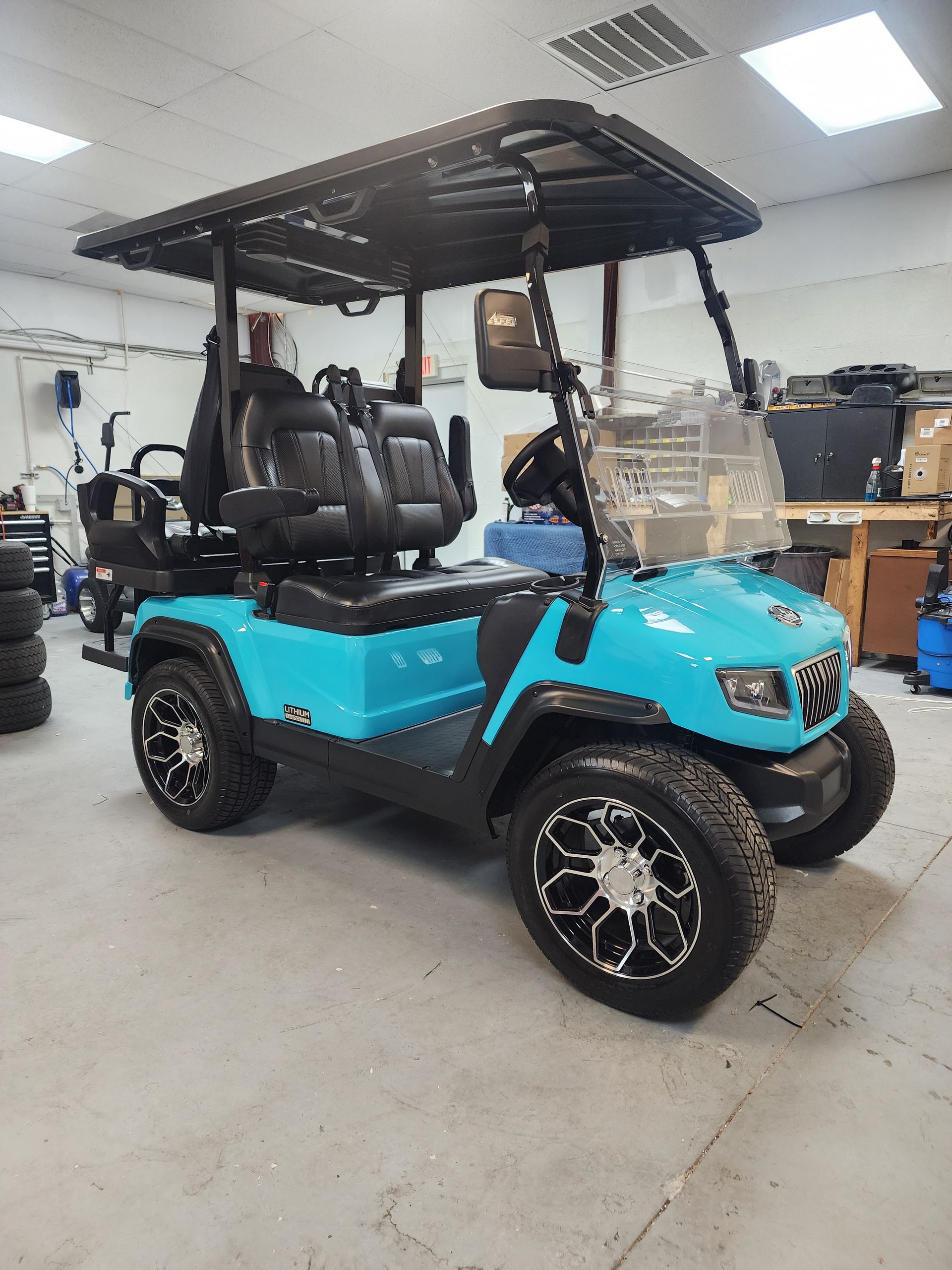 Teal golf cart with black roof, seats, and wheels, parked indoors.