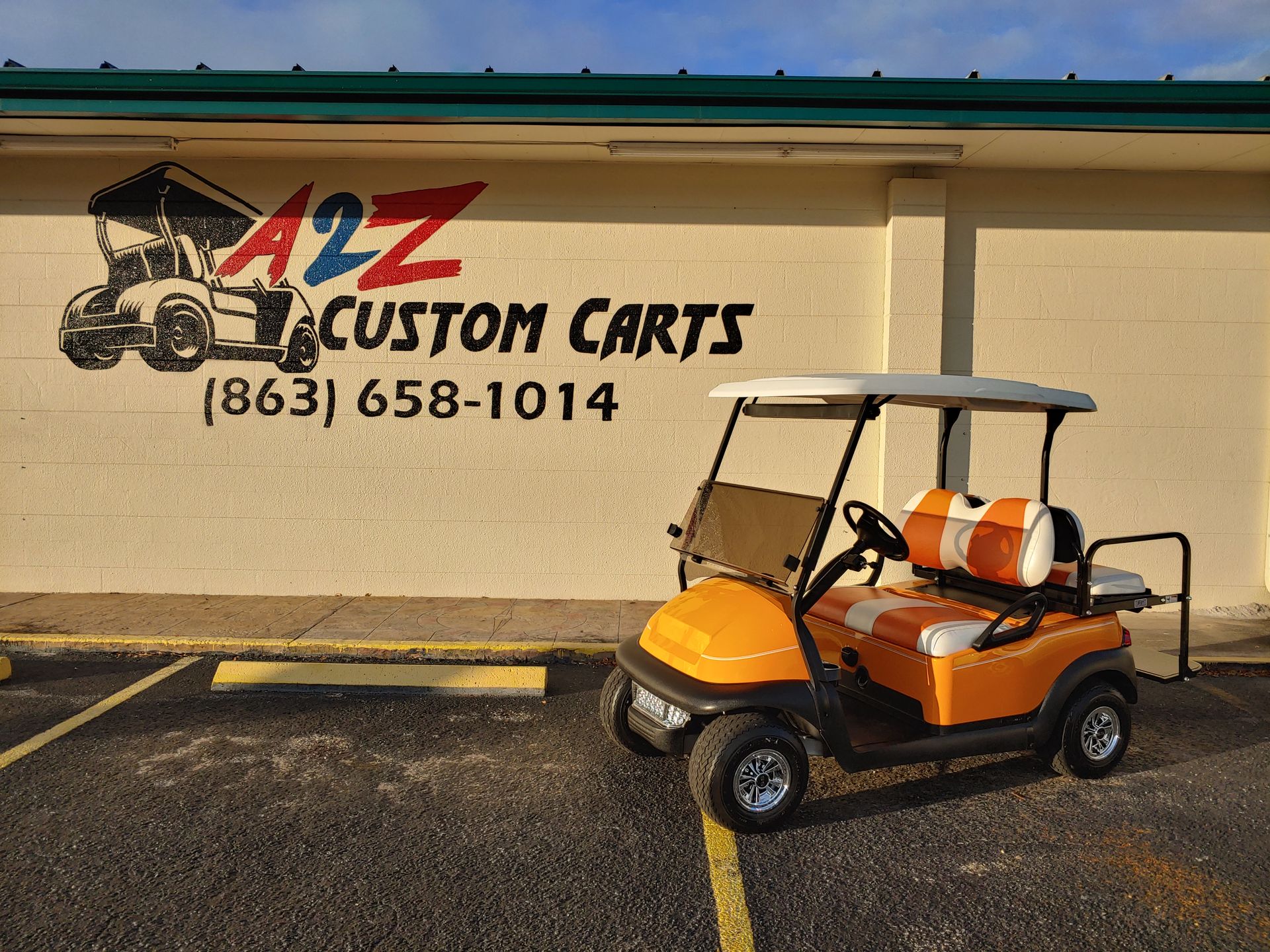 Orange golf cart parked in front of A2Z Custom Carts sign on a tan building.