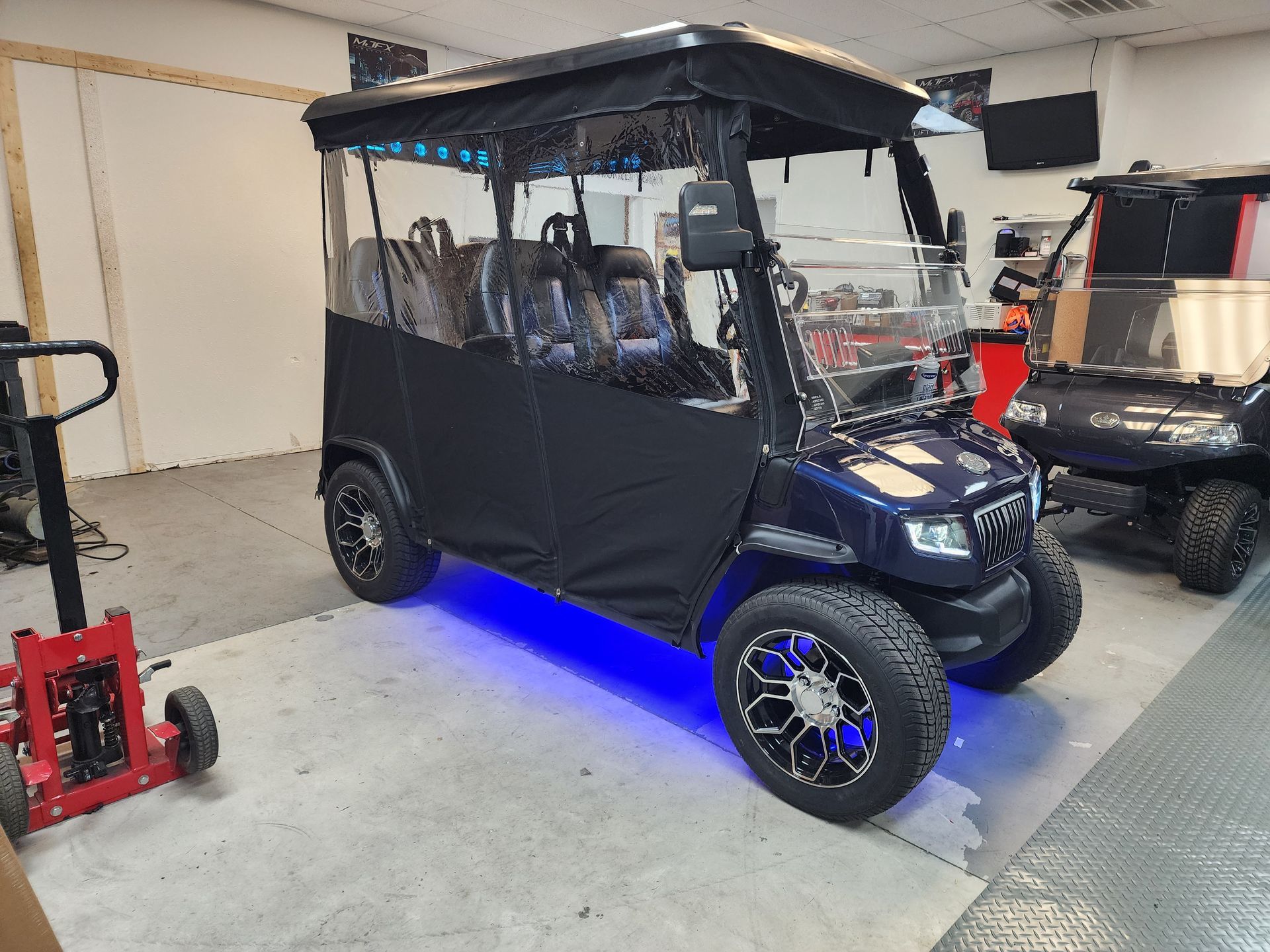 Dark blue golf cart with black enclosure and blue underglow, parked in a garage.
