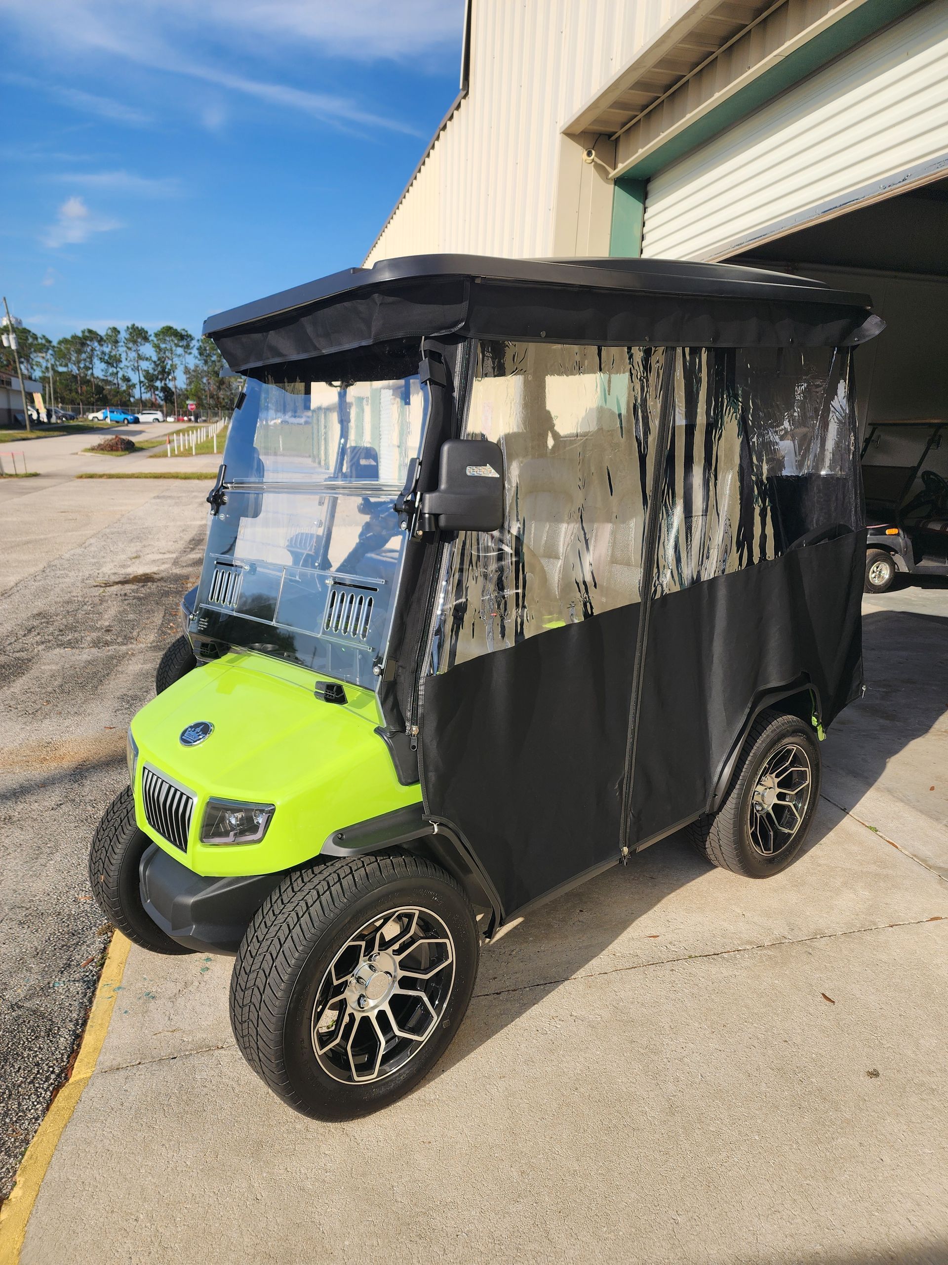 Green golf cart with black enclosure, parked on concrete. Sunny outdoor setting.
