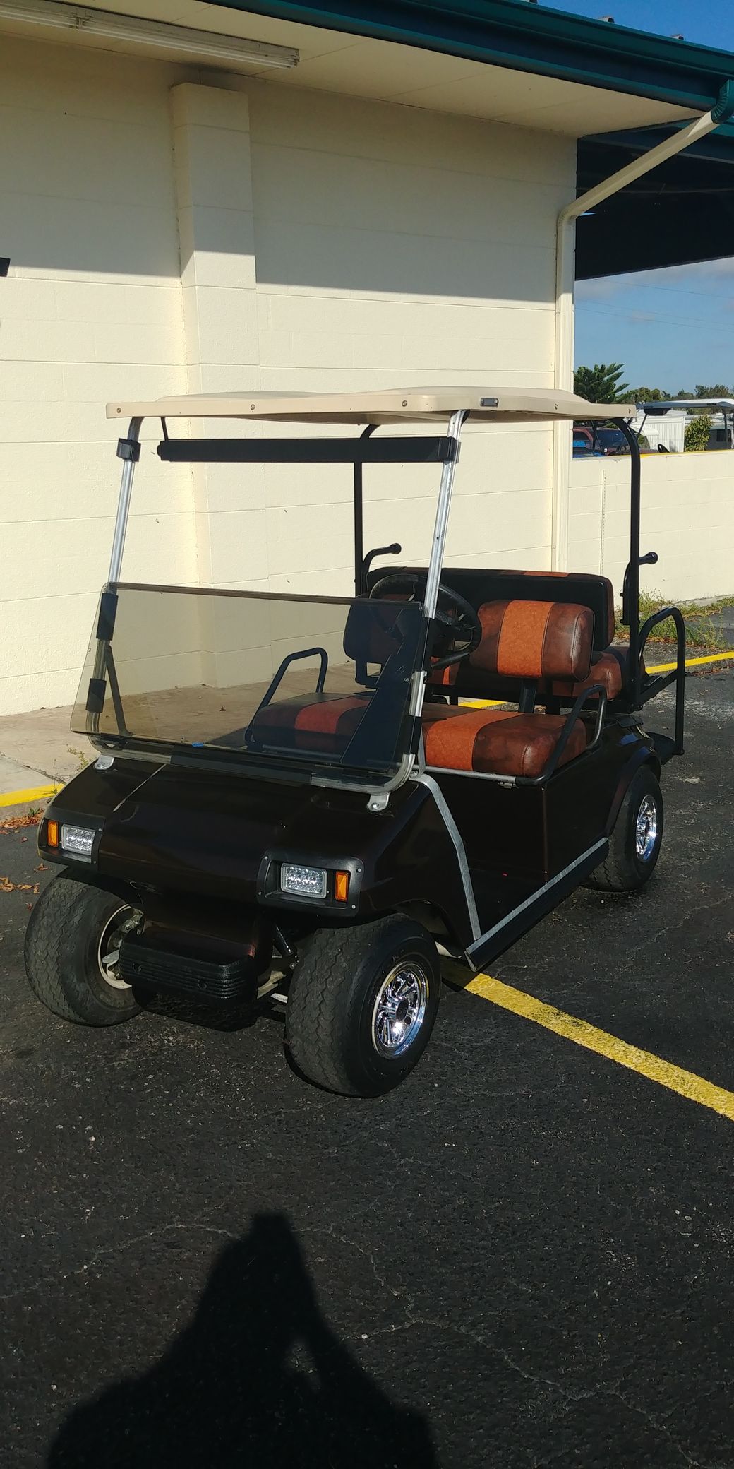 Black golf cart with orange seats parked outside building on asphalt.