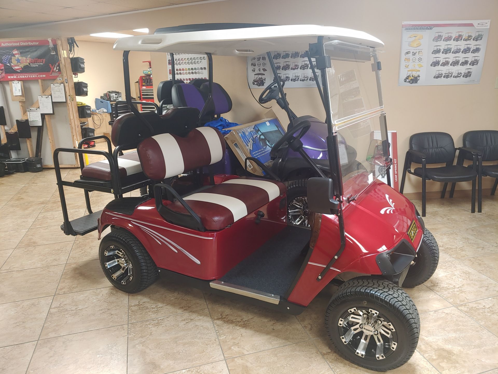 Red golf cart with white roof, maroon and white seats, and black tires parked indoors.