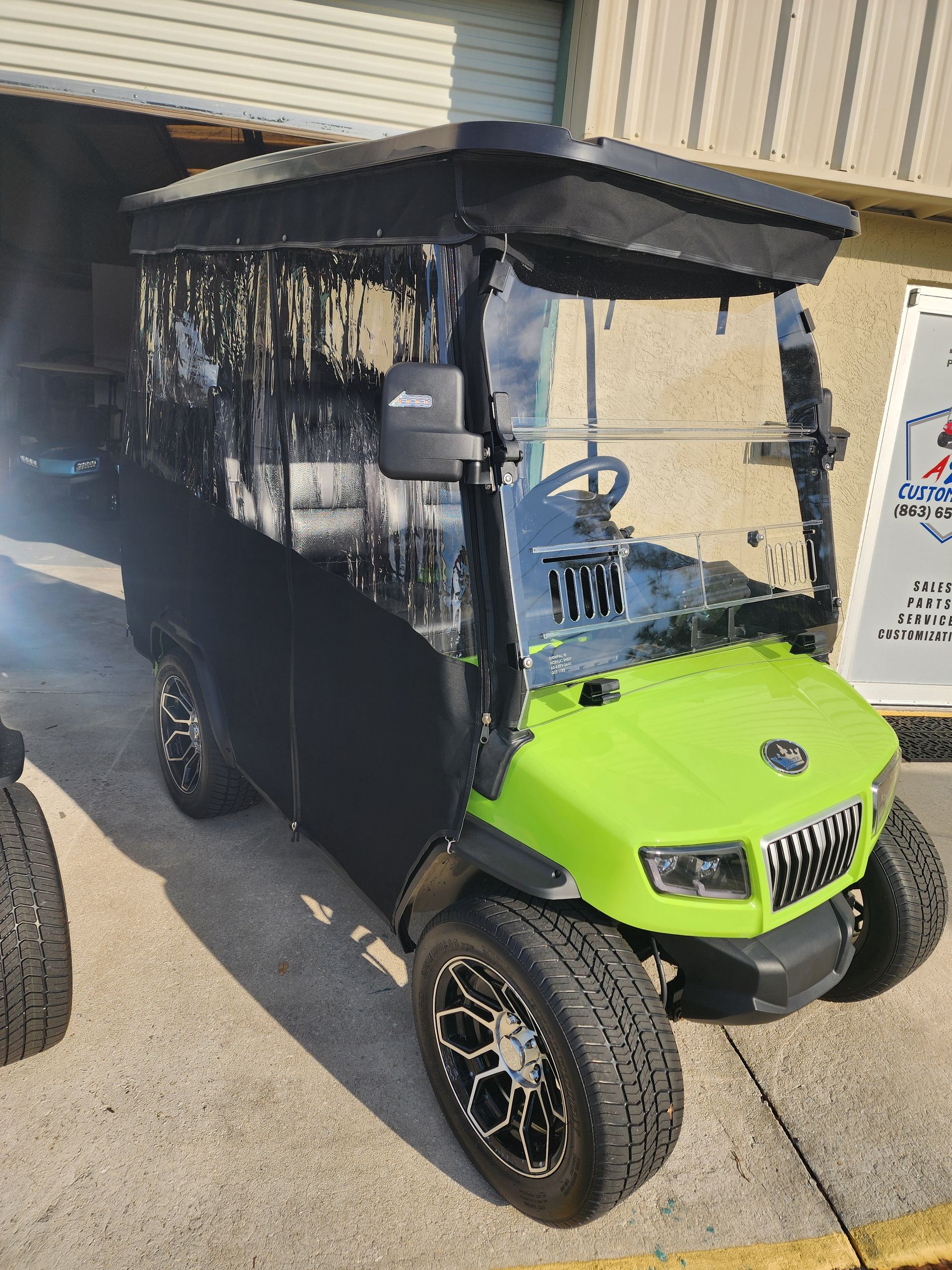 Green and black golf cart with clear side curtains parked outside a building.