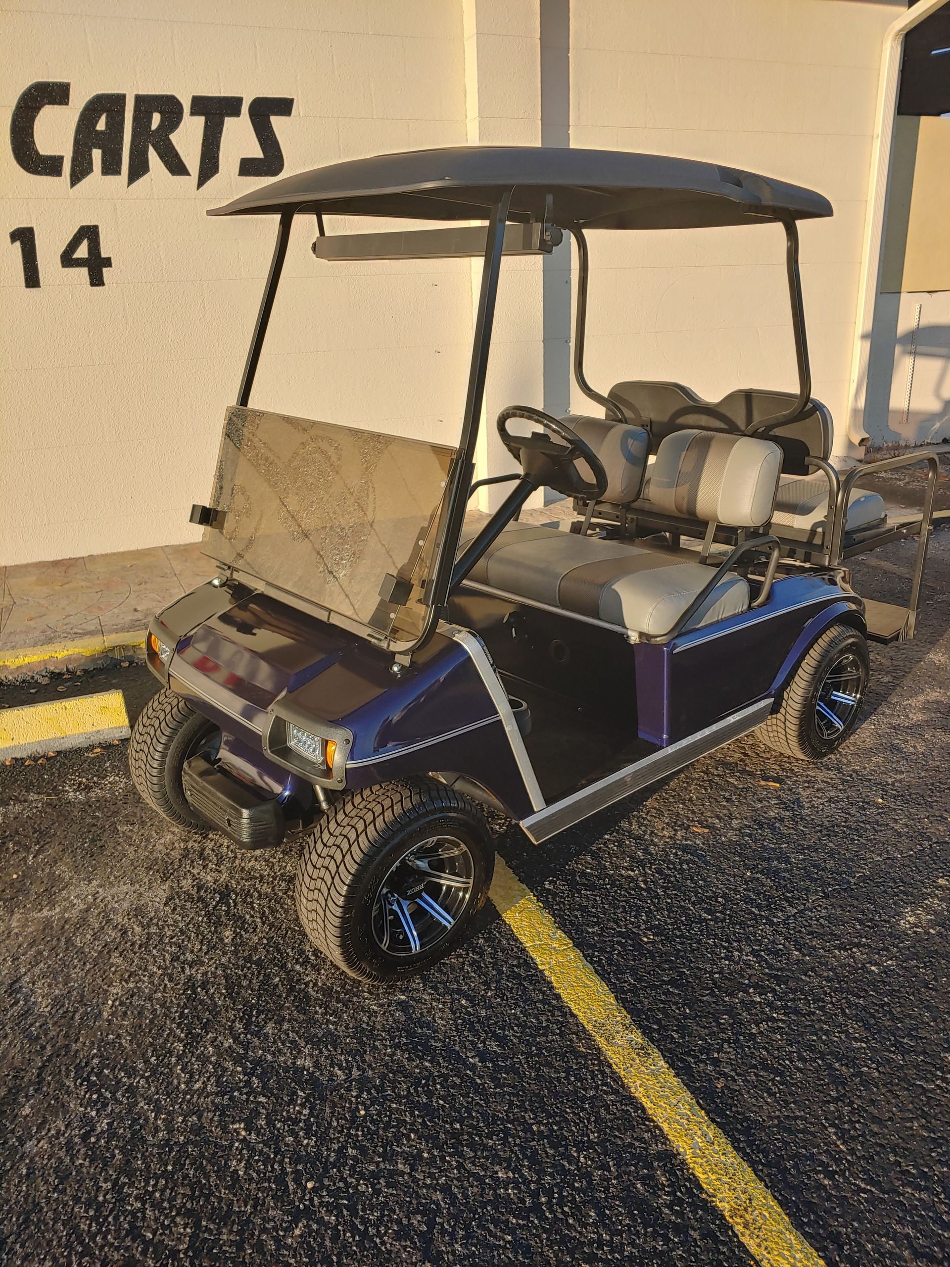 Purple and black golf cart parked outside, with black wheels, and a canopy.