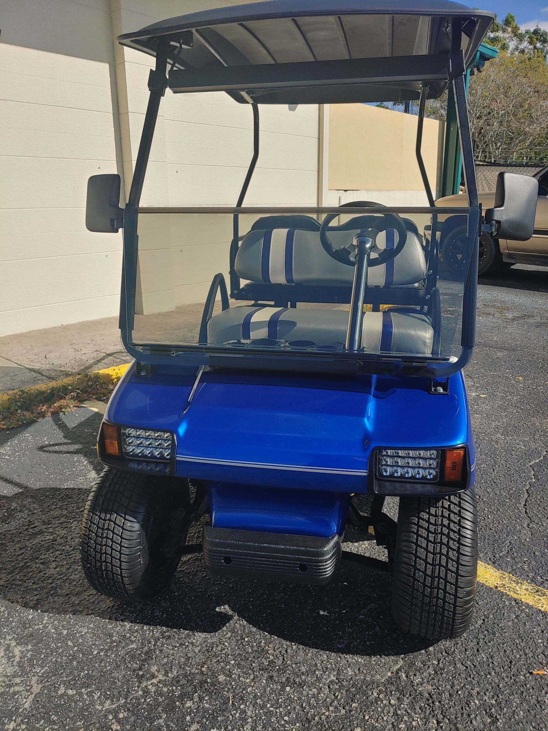 Blue golf cart with a windshield, canopy, and black tires parked outside.