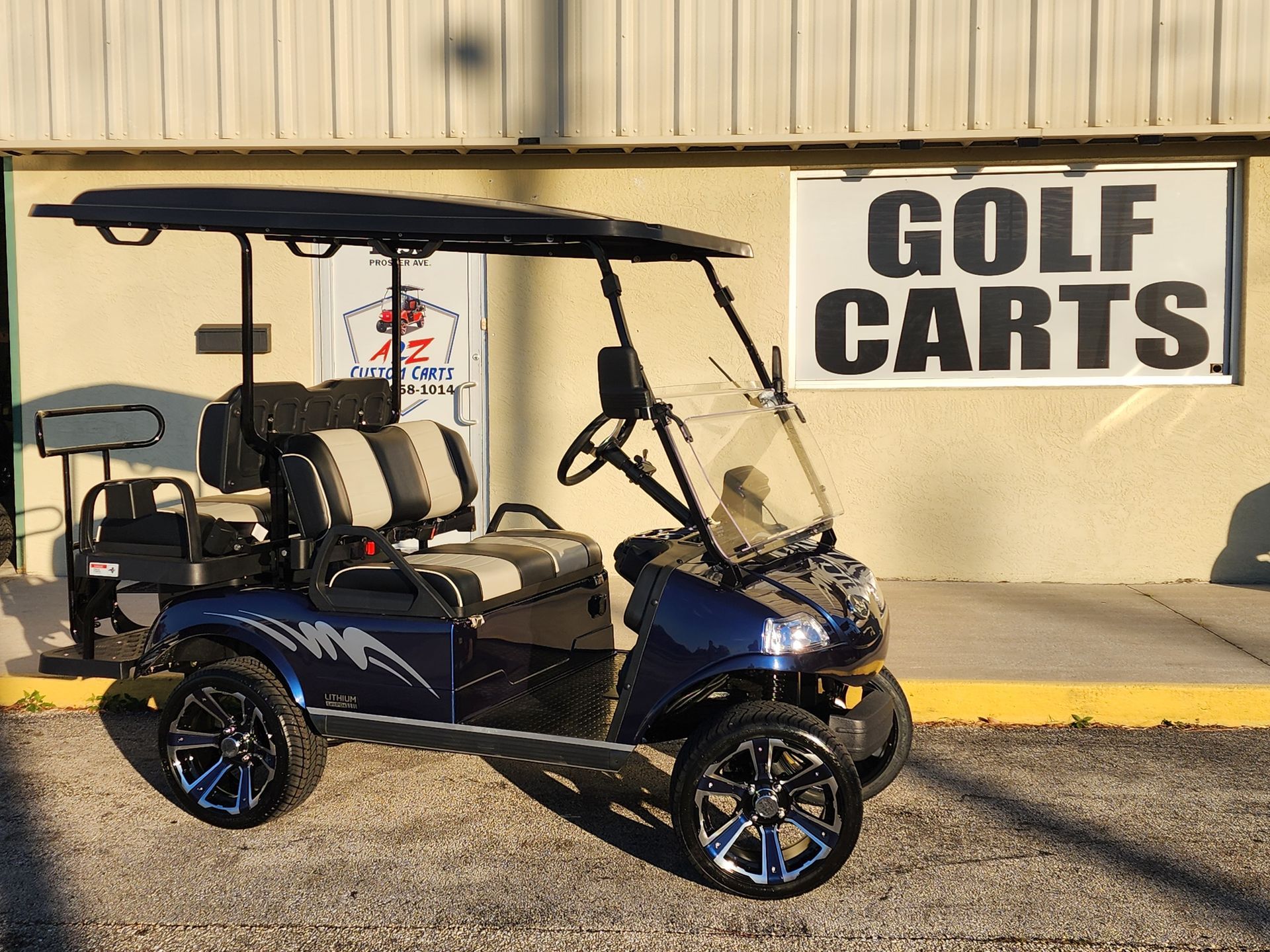 Blue golf cart with black roof, custom wheels, and windshield parked in front of a 