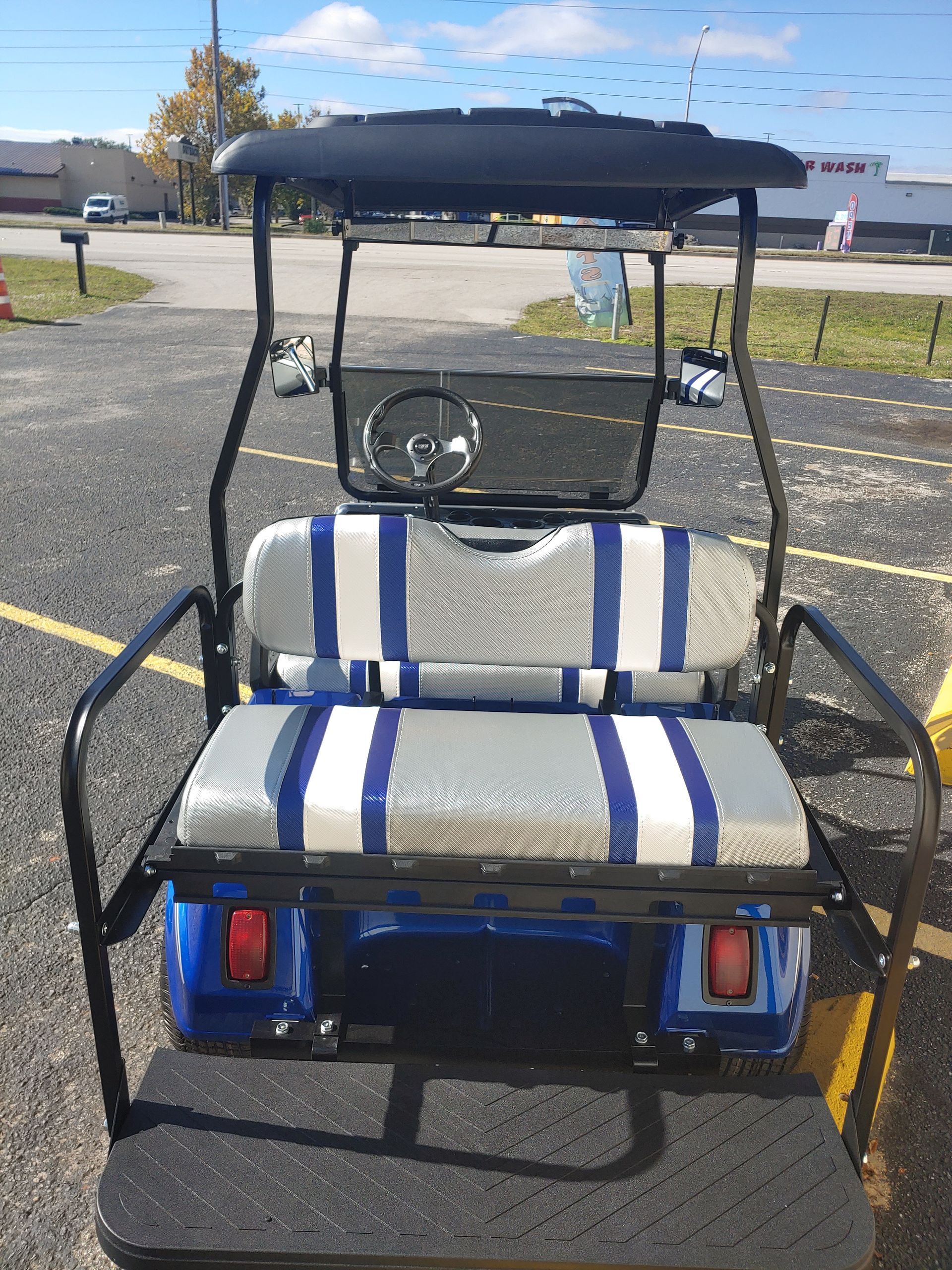 Blue golf cart with black frame, striped seats, and a black roof. Outdoors.