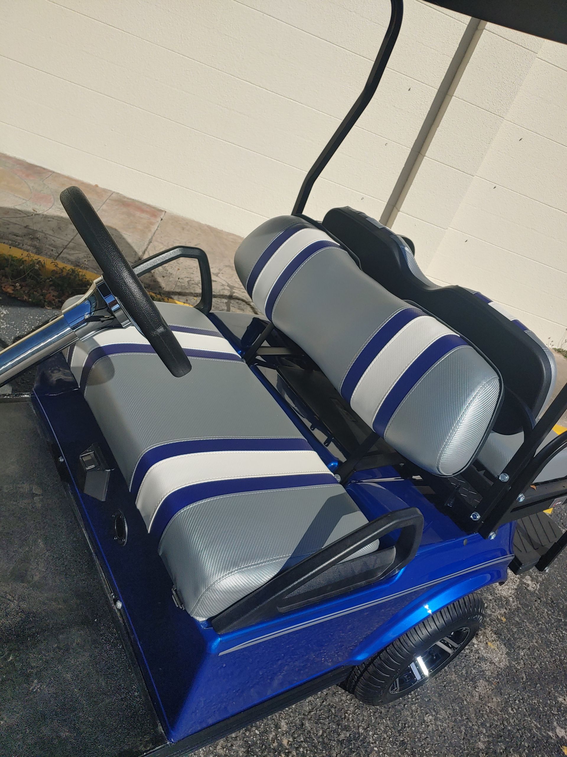 Blue golf cart with gray, white, and blue seats parked outside.