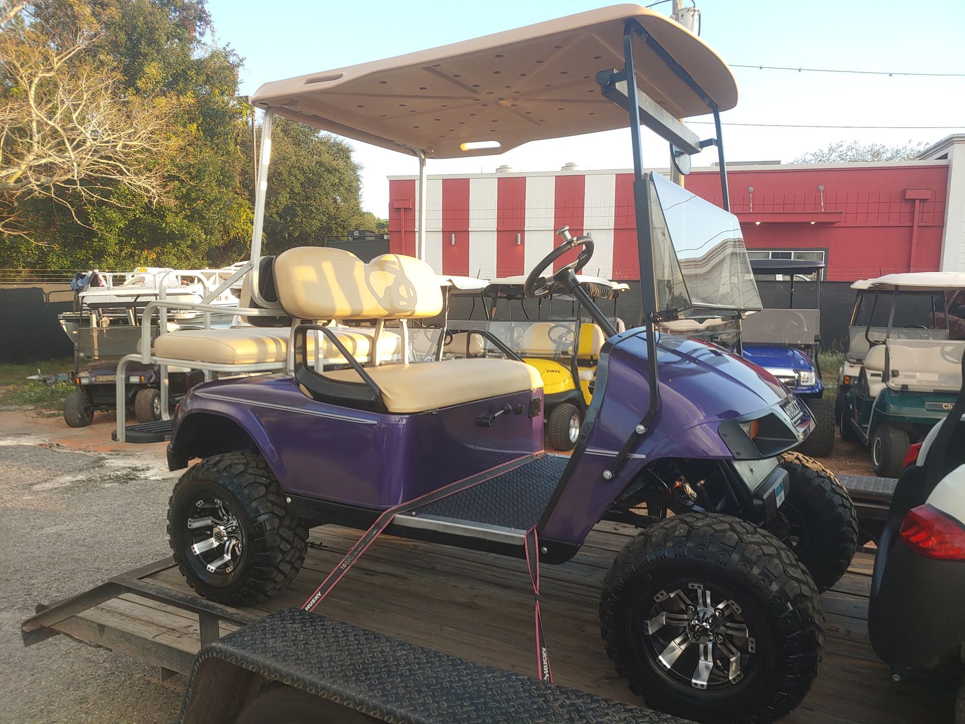 Purple golf cart with tan seats and roof, on a trailer.