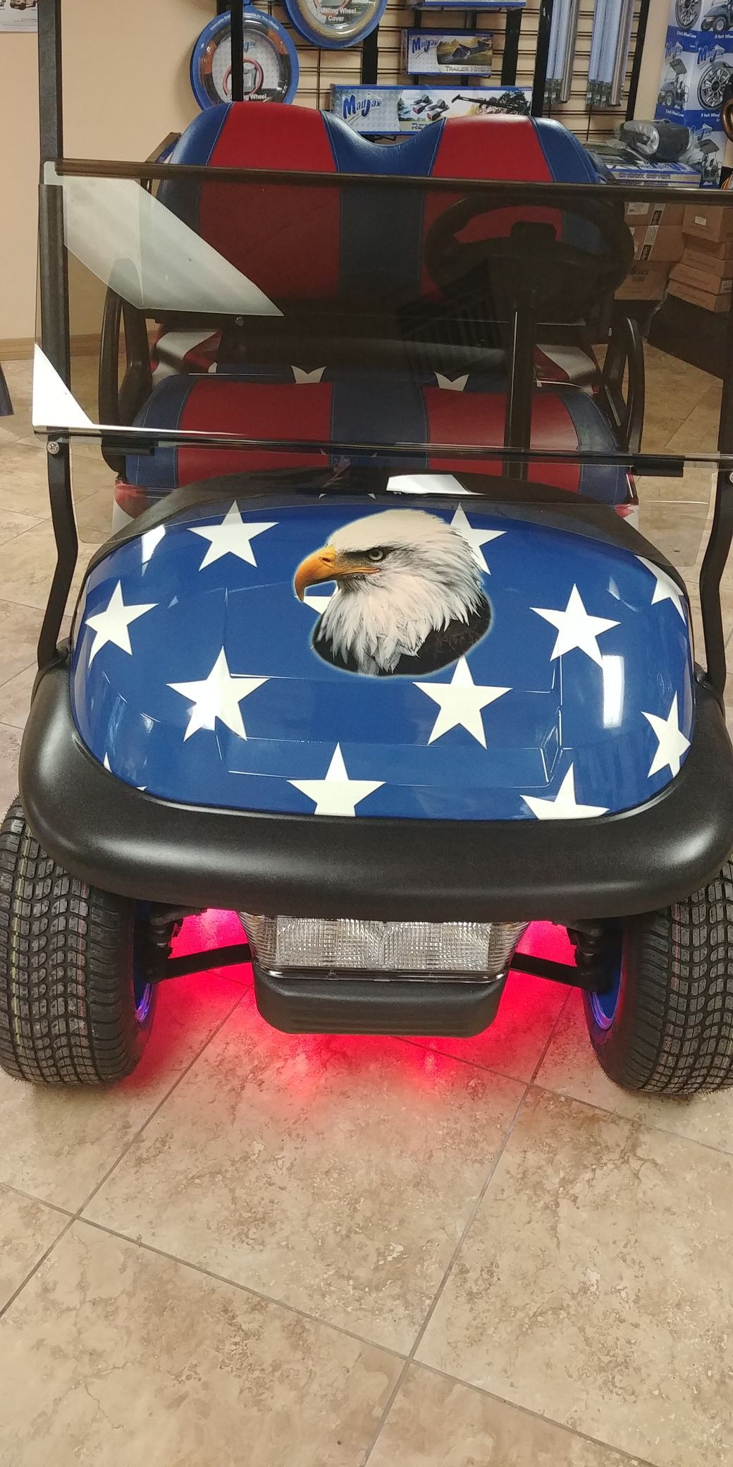 Patriotic golf cart with blue stars, eagle head, red underglow, and off-road tires.