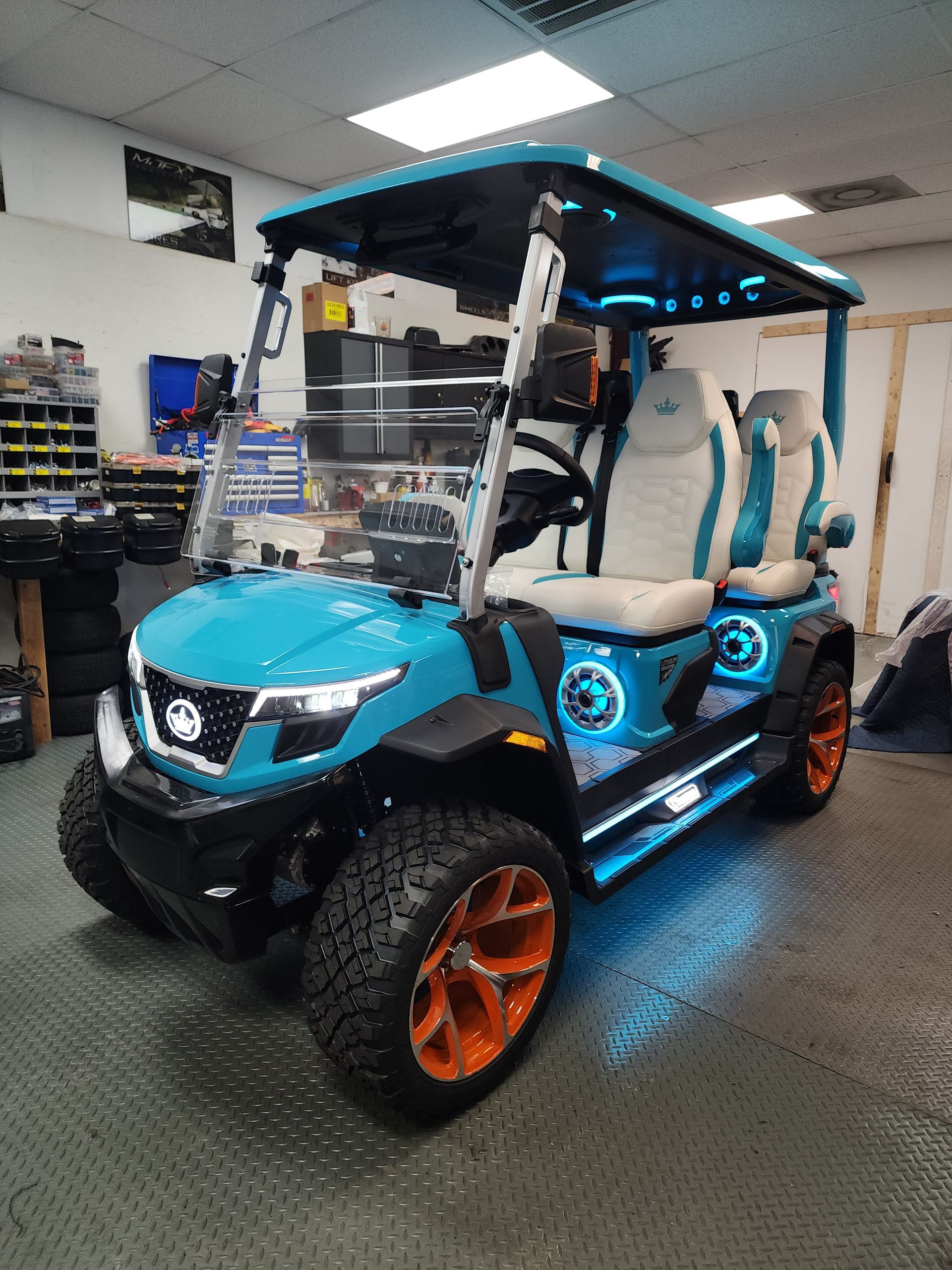 Teal and orange customized golf cart with LED lights, parked indoors.