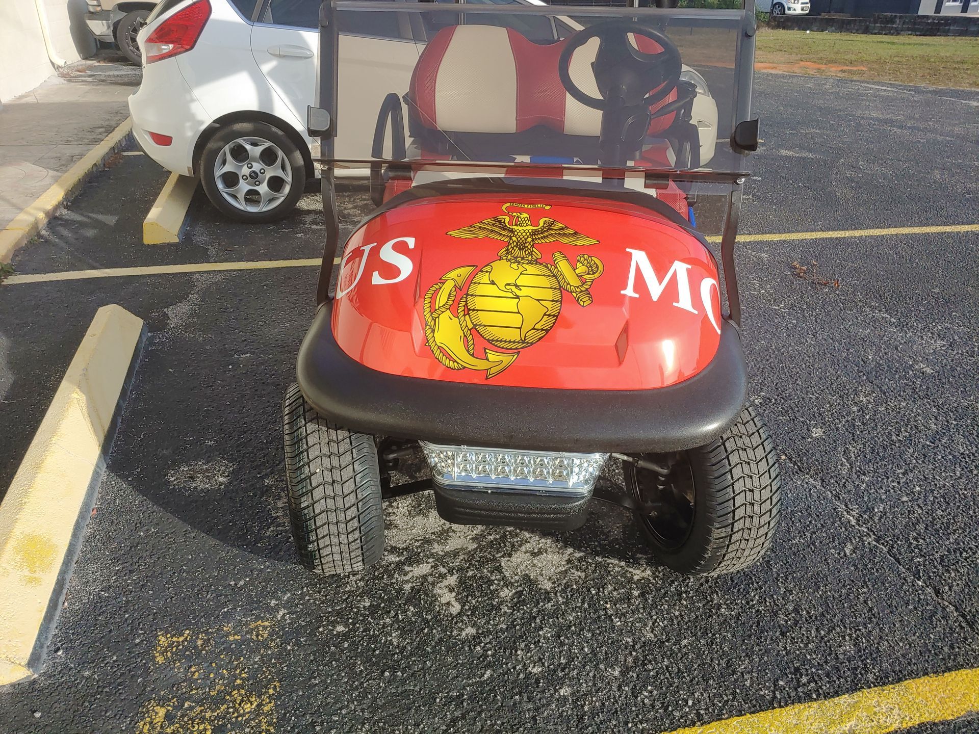 Red golf cart with US Marine Corps logo parked on asphalt.