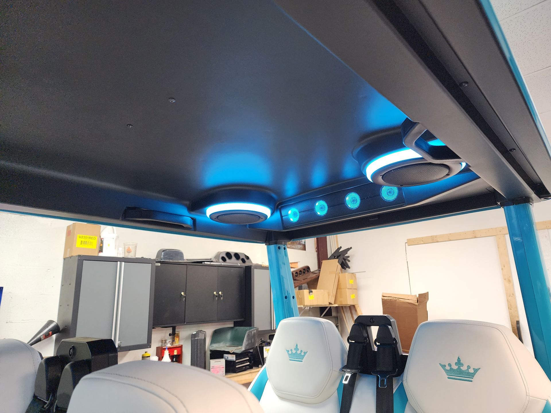 Interior view of a UTV with blue lit speakers on the ceiling and white seats.