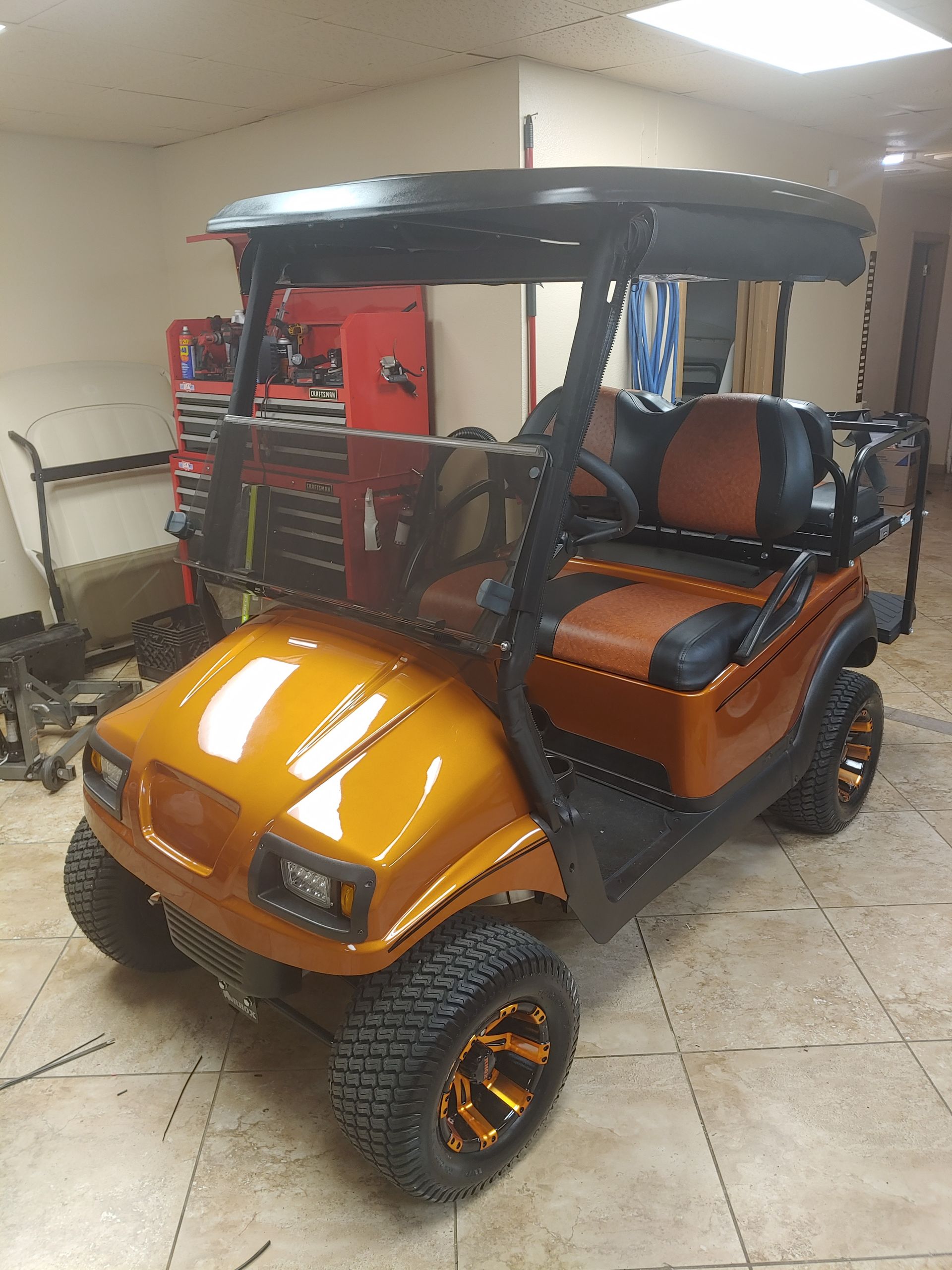 Orange golf cart with black roof and wheels, inside a garage.