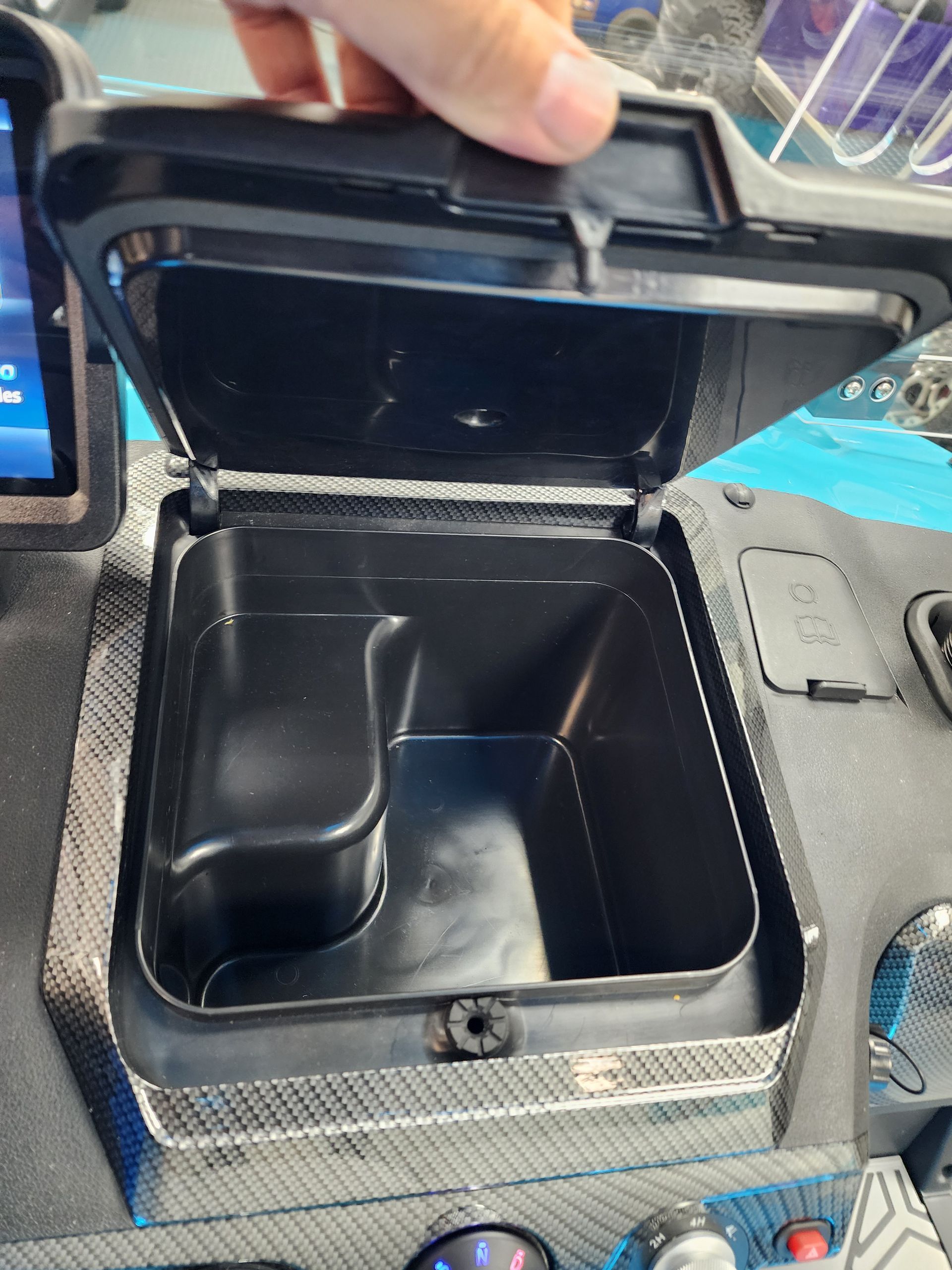 Hand opening a black compartment in a vehicle's dashboard, revealing an empty storage area.