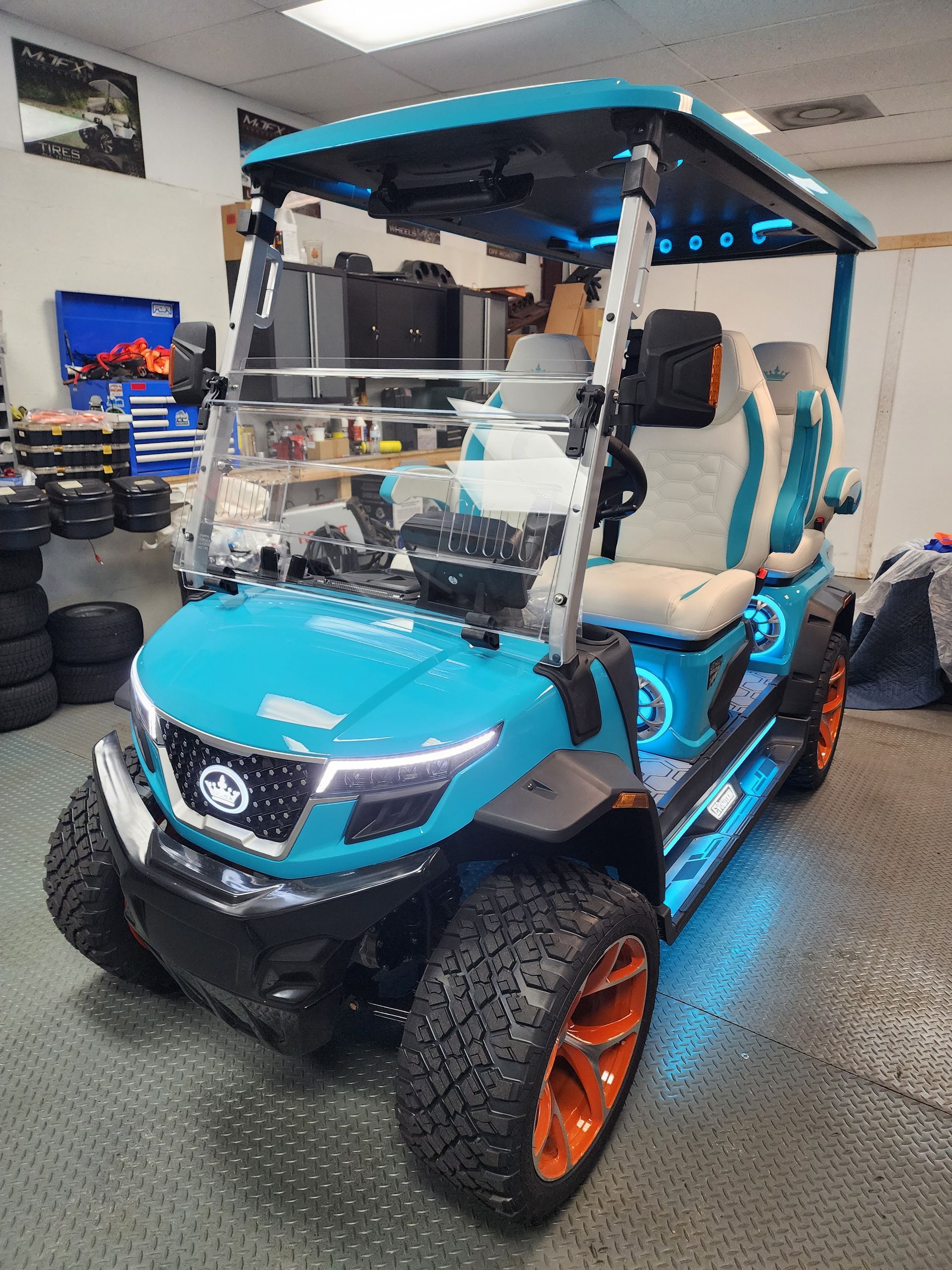 Custom teal golf cart with orange accents and LED lights, indoors.