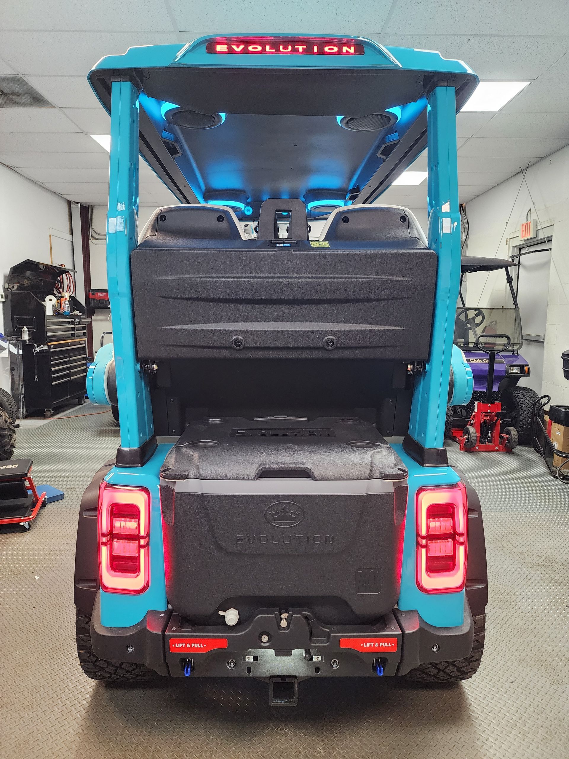 Rear view of a turquoise Evolution golf cart with black storage boxes and LED lights.
