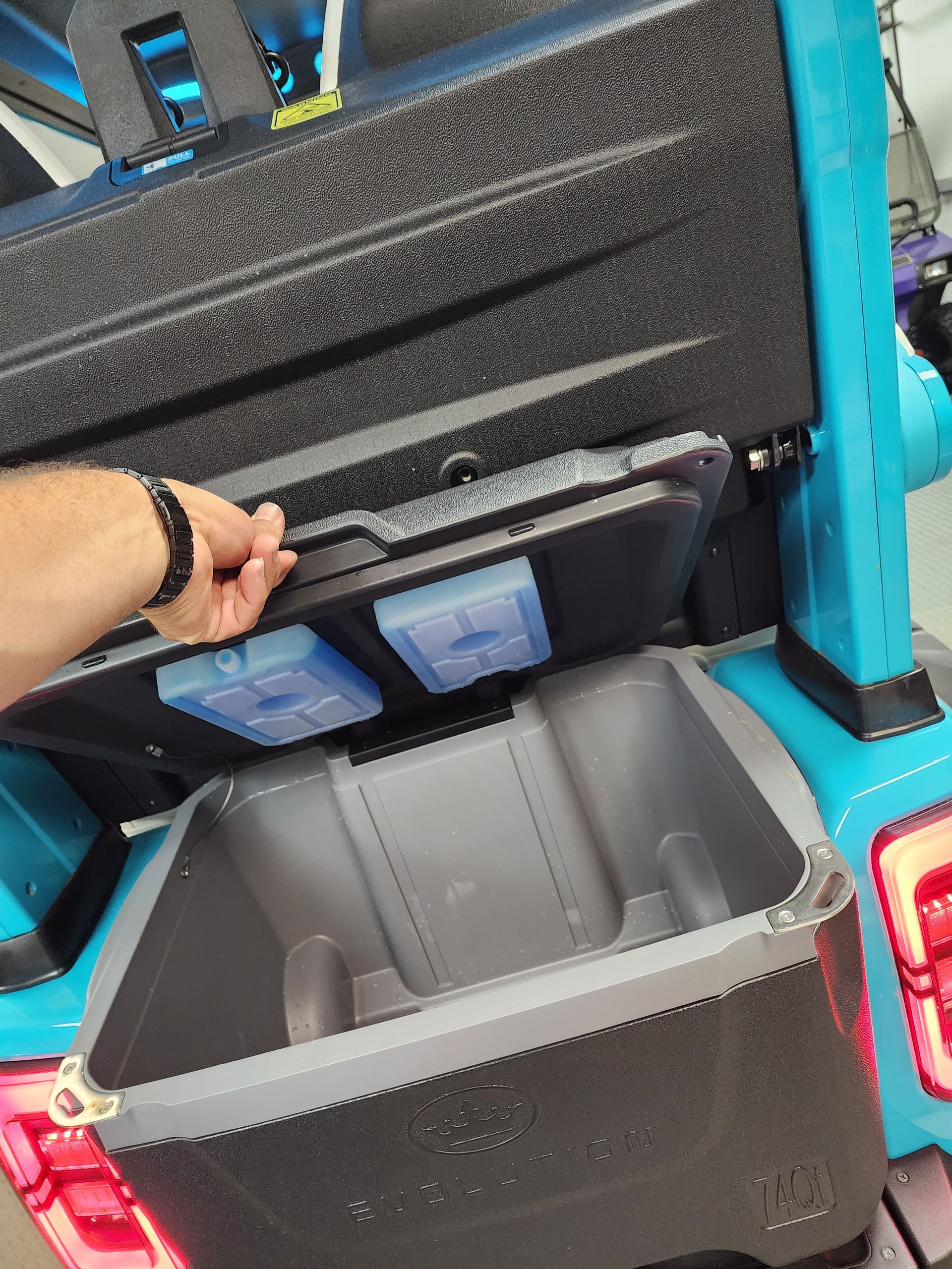 Hand lifting a tray in a turquoise cooler, revealing a compartment with ice packs.