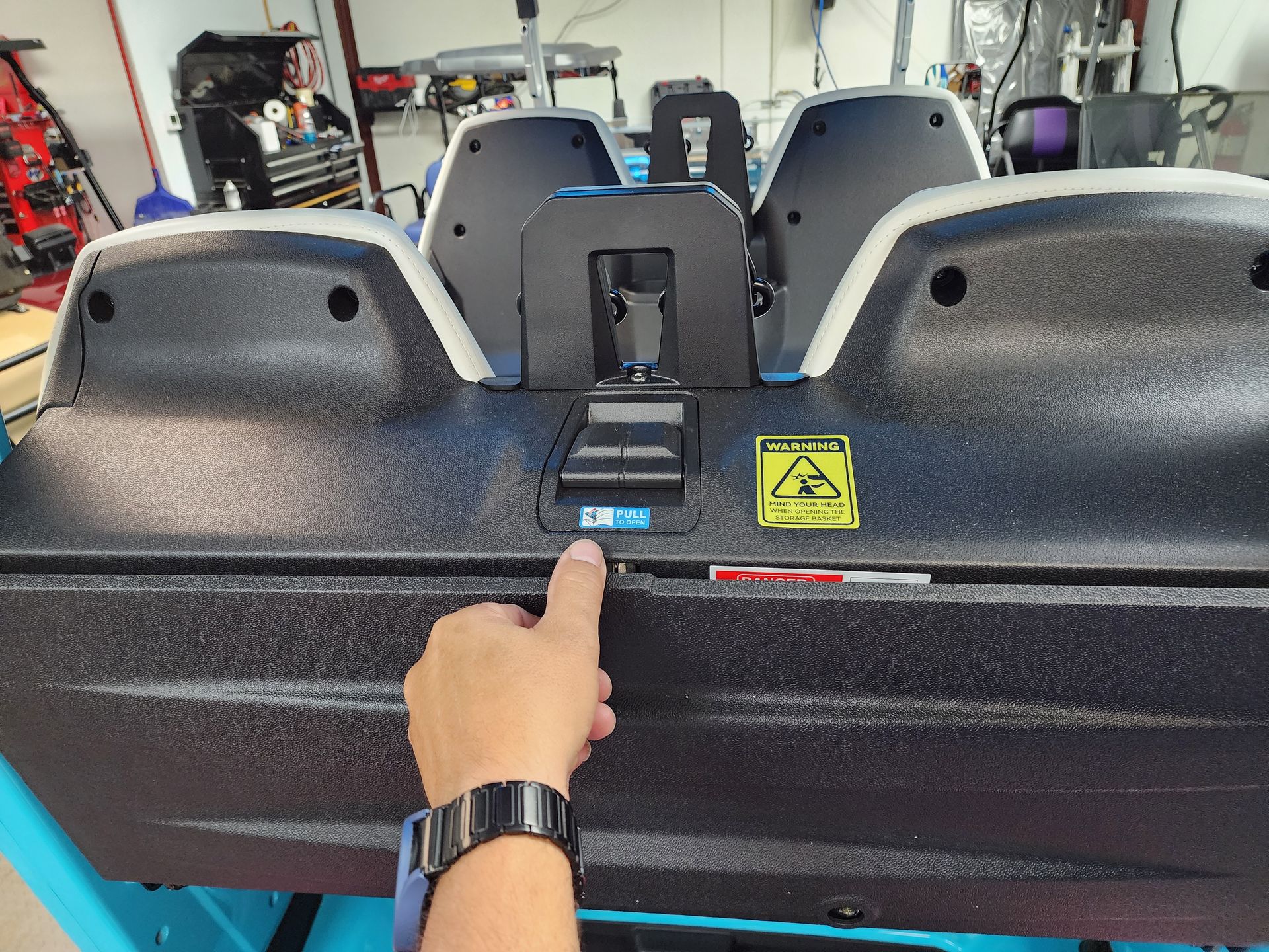 Hand pointing at a blue label on a machine's black and white textured surface; warning sign visible.